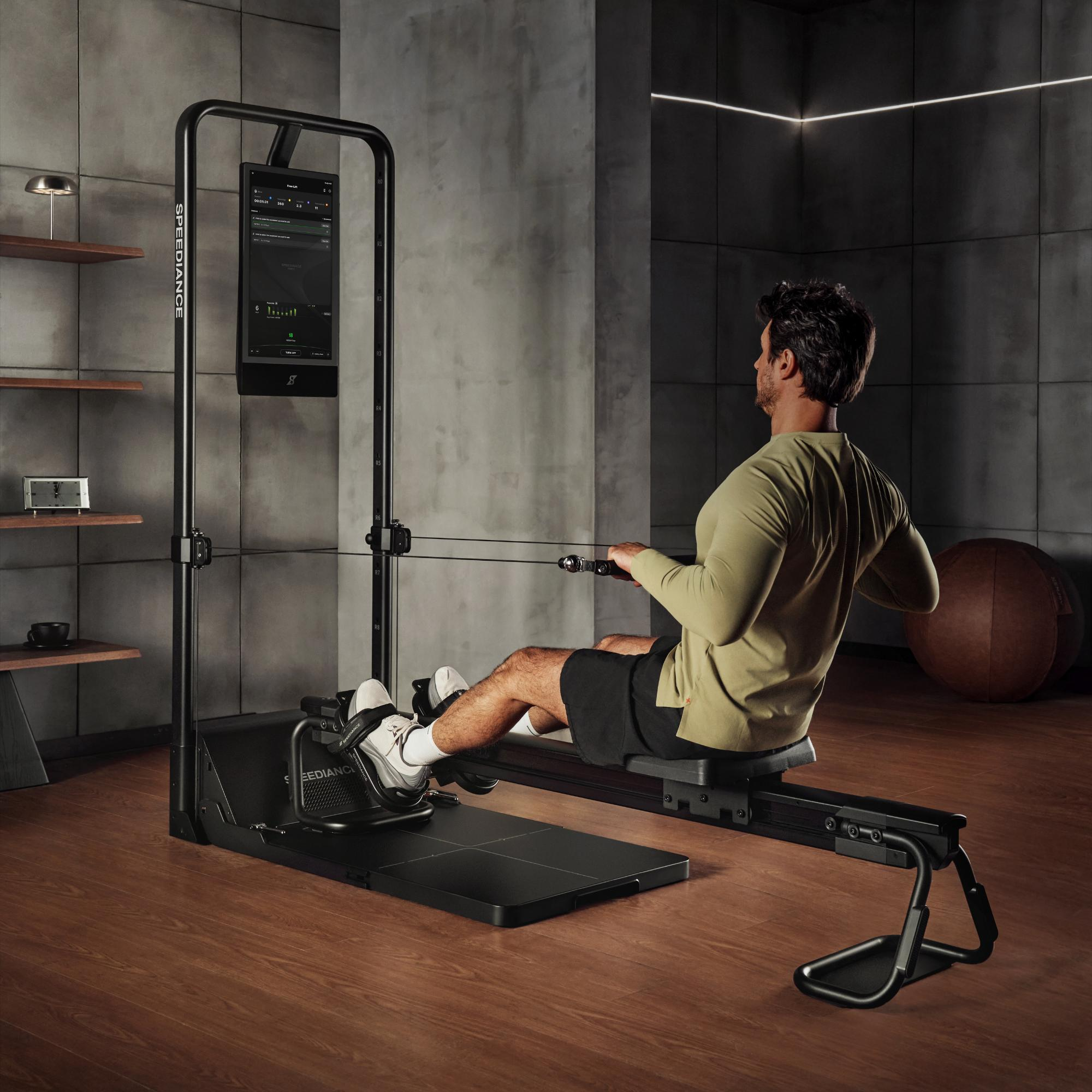 Man roeit op zwarte hometrainer voor grijs beton en donkere wandpanelen.