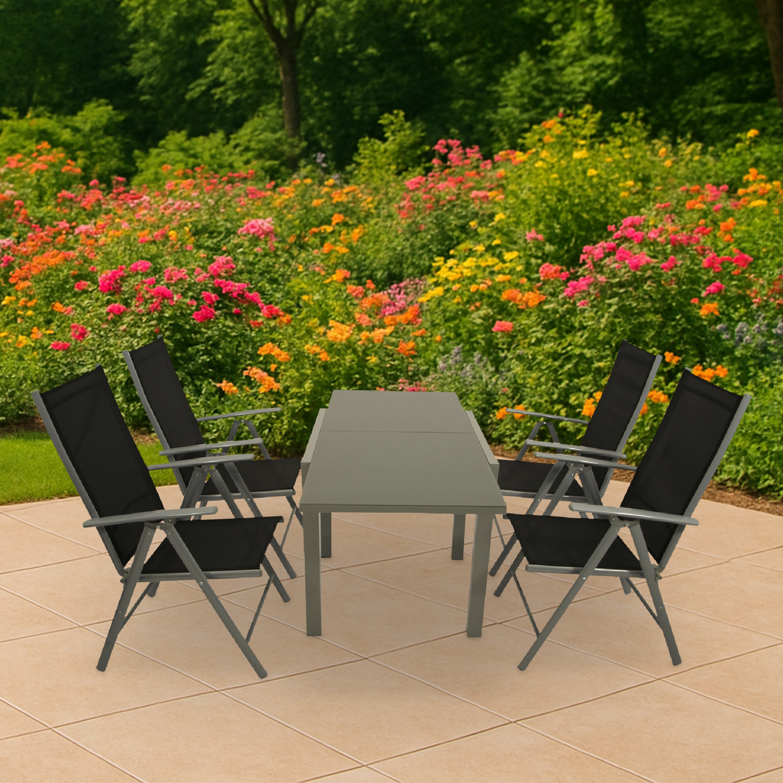 Ein grauer Tisch mit vier schwarzen Stühlen steht auf einer gefliesten Terrasse vor blühenden Blumen.