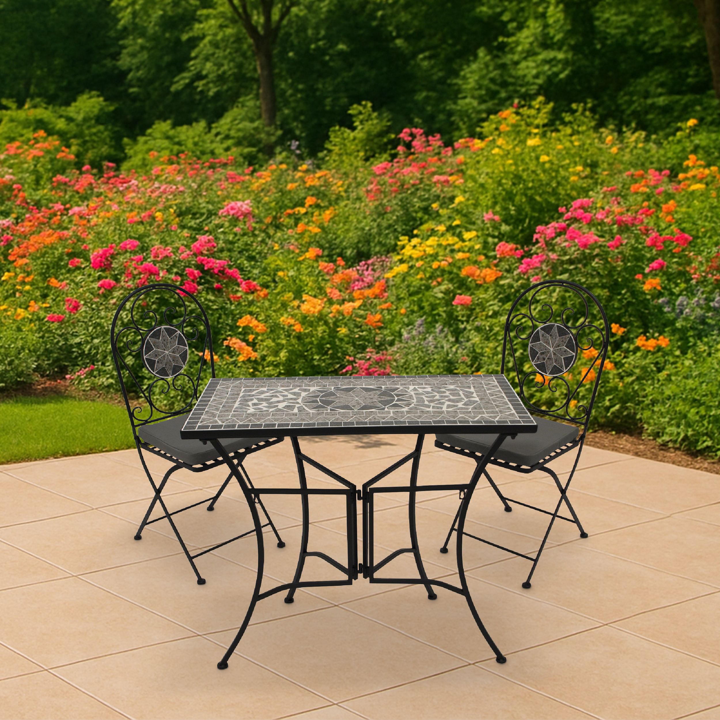 Ein Mosaiktisch mit zwei Stühlen steht auf einer Terrasse vor blühenden Blumen.