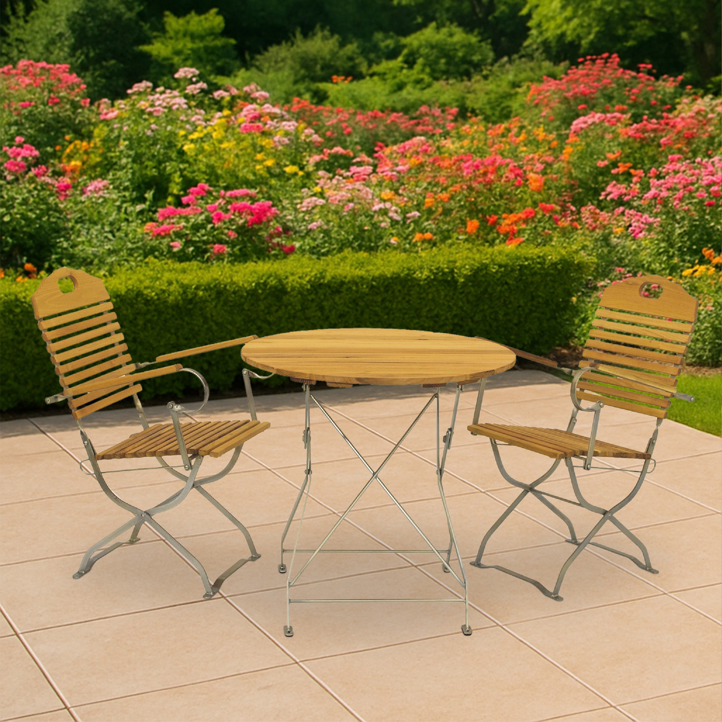 Holztisch und zwei Stühle auf einer Terrasse mit Blumenbeeten im Hintergrund.