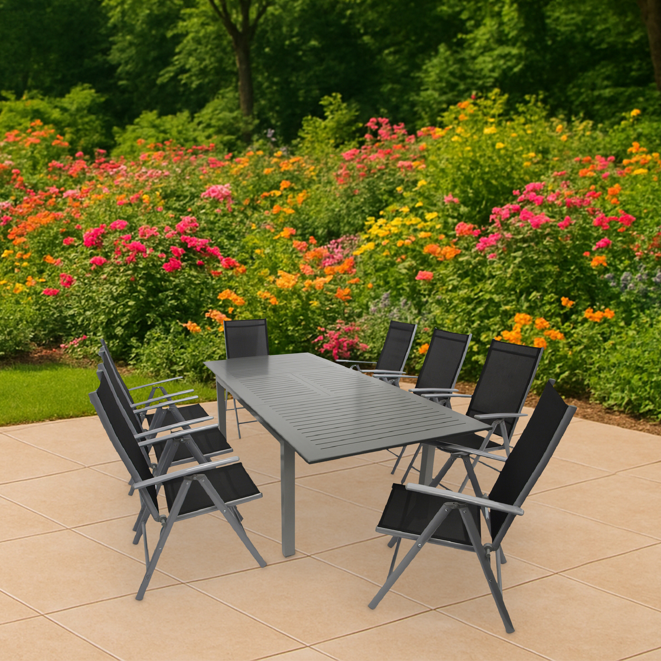 Ein grauer Tisch mit schwarzen Stühlen steht auf einer Terrasse vor blühenden Blumen.