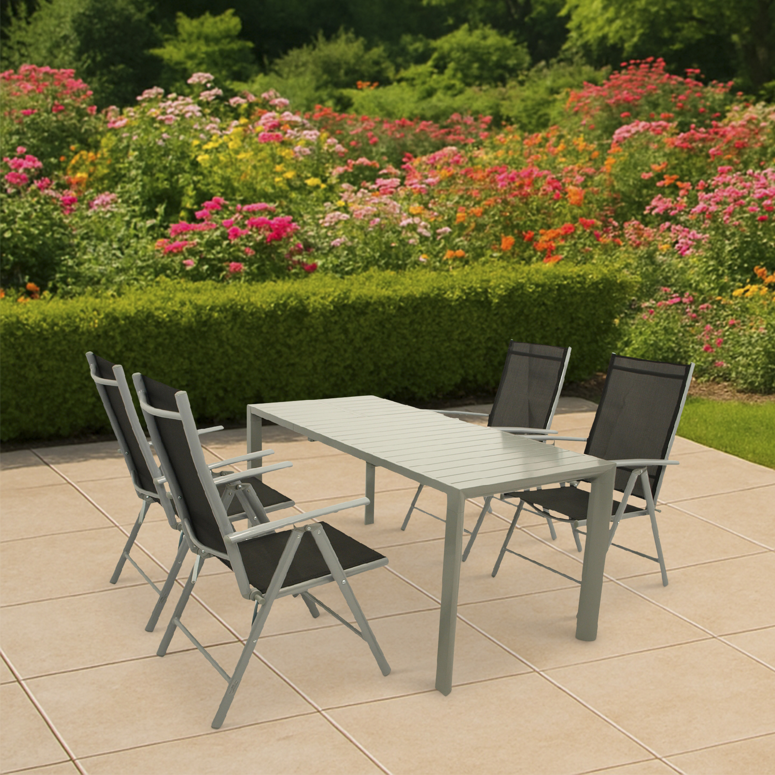 Ein Tisch mit vier Stühlen auf einer Terrasse vor einem blühenden Garten.