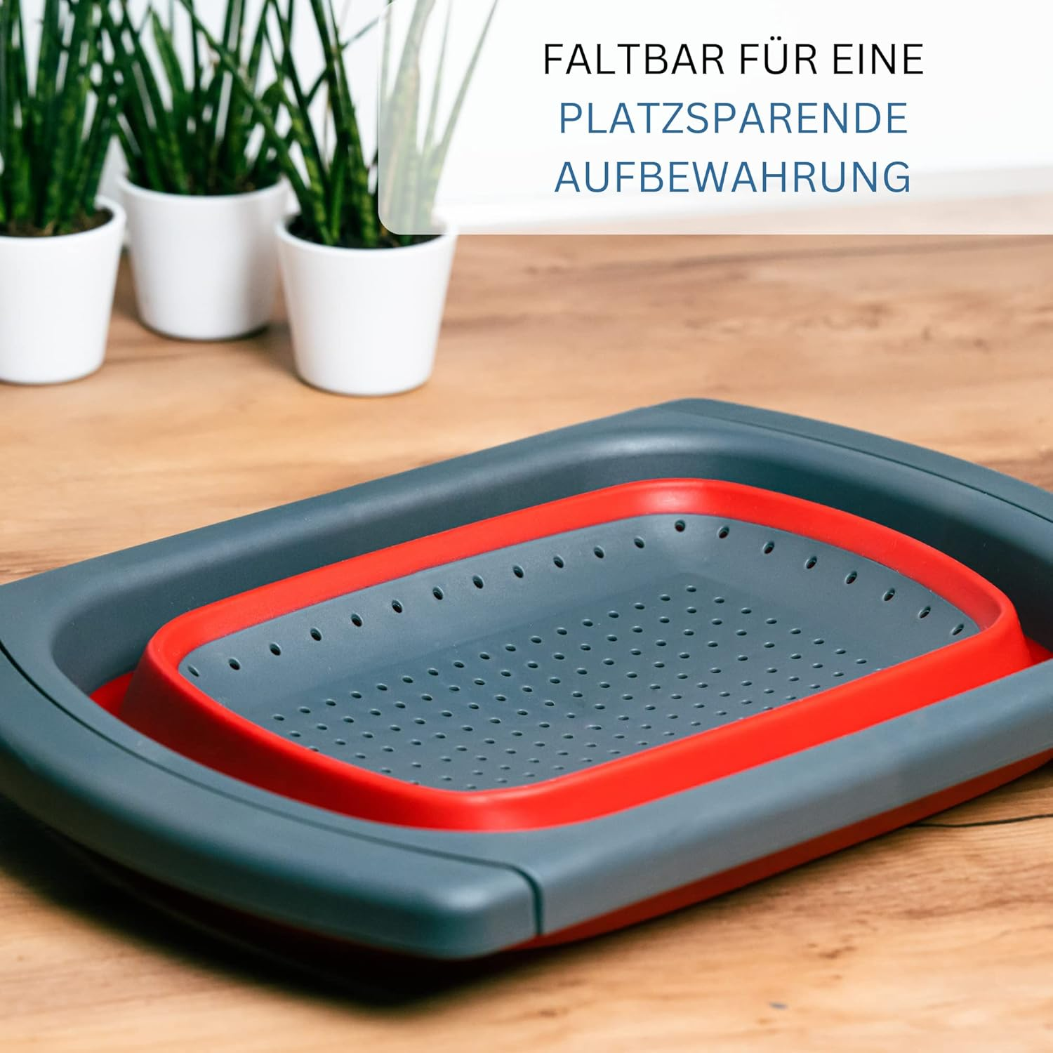 Graue und rote faltbare Abtropfschale mit Löchern auf Holztisch.