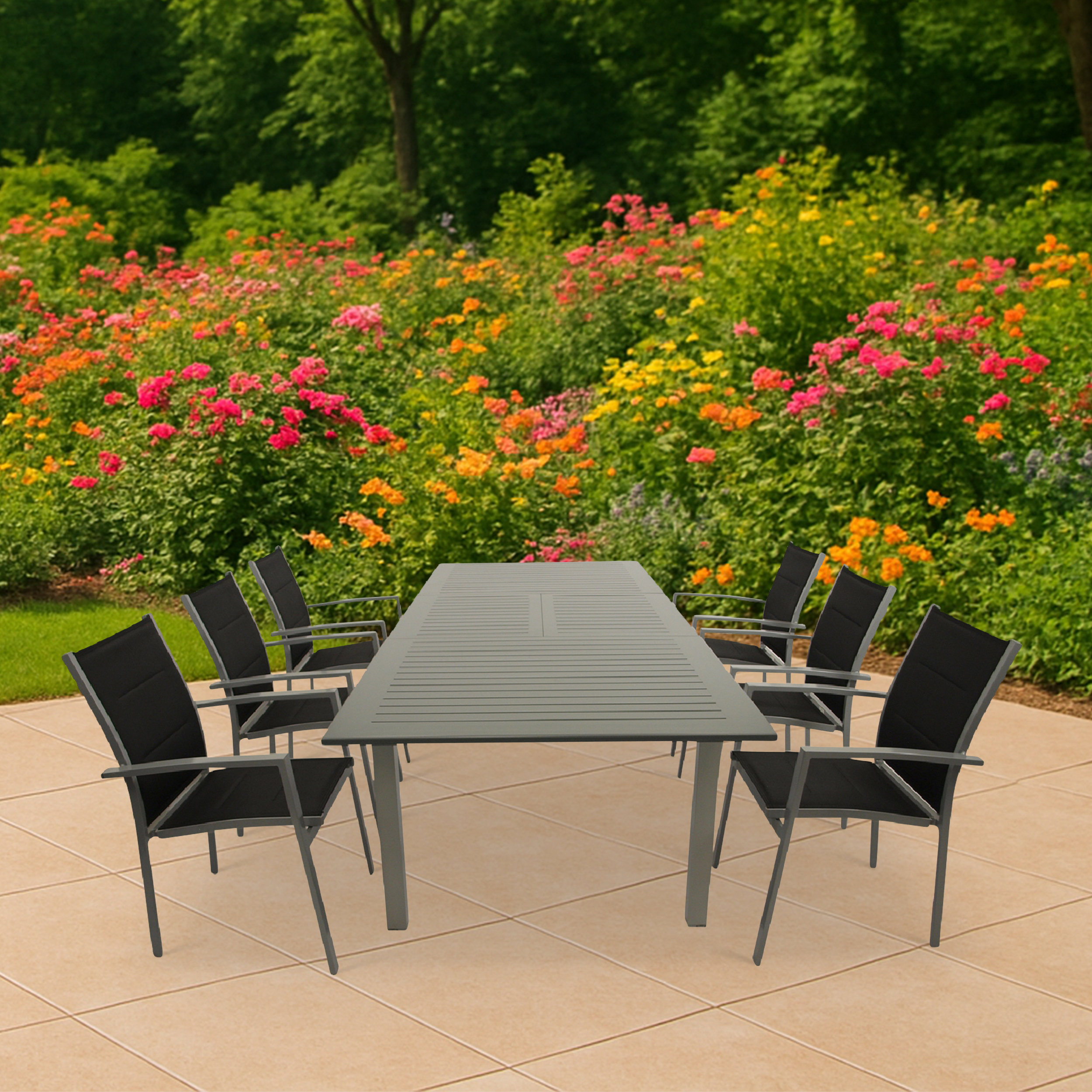 Ein grauer Tisch mit schwarzen Stühlen steht auf einer gefliesten Terrasse, umgeben von Blumen.