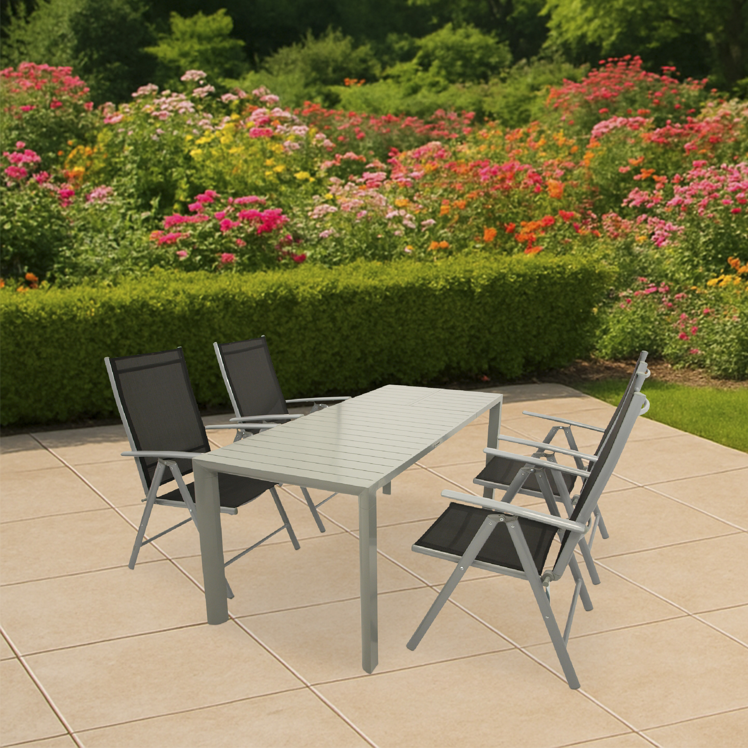 Ein grauer Tisch mit vier schwarzen Stühlen auf einer gefliesten Terrasse, umgeben von blühenden Rosenbüschen.