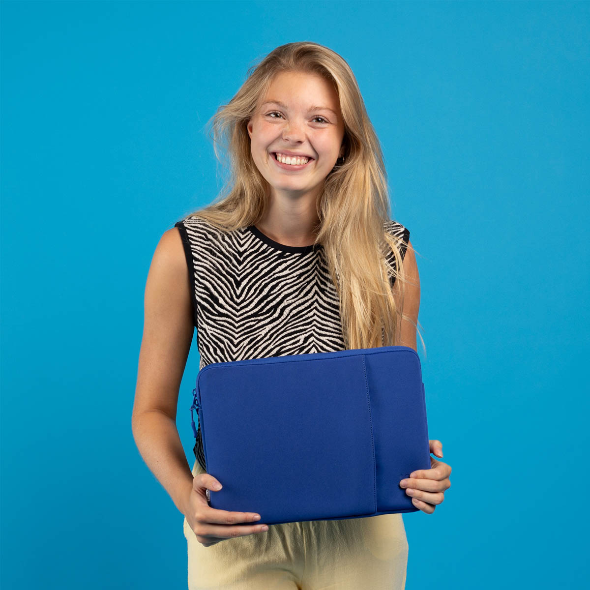 A smiling young woman with long blonde hair holds a blue laptop sleeve.
