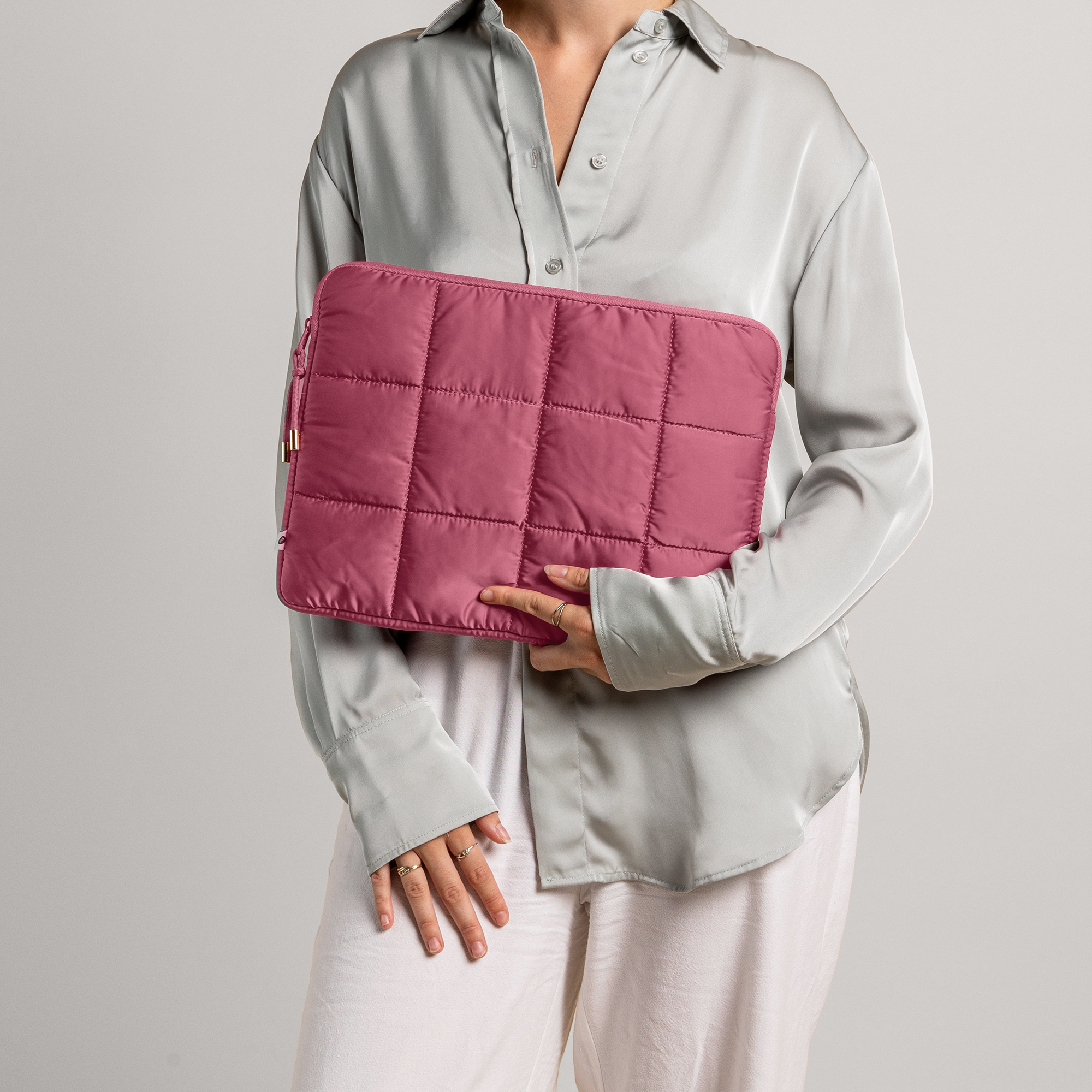 Woman holding a quilted, dusty rose laptop sleeve and a grey satin shirt.