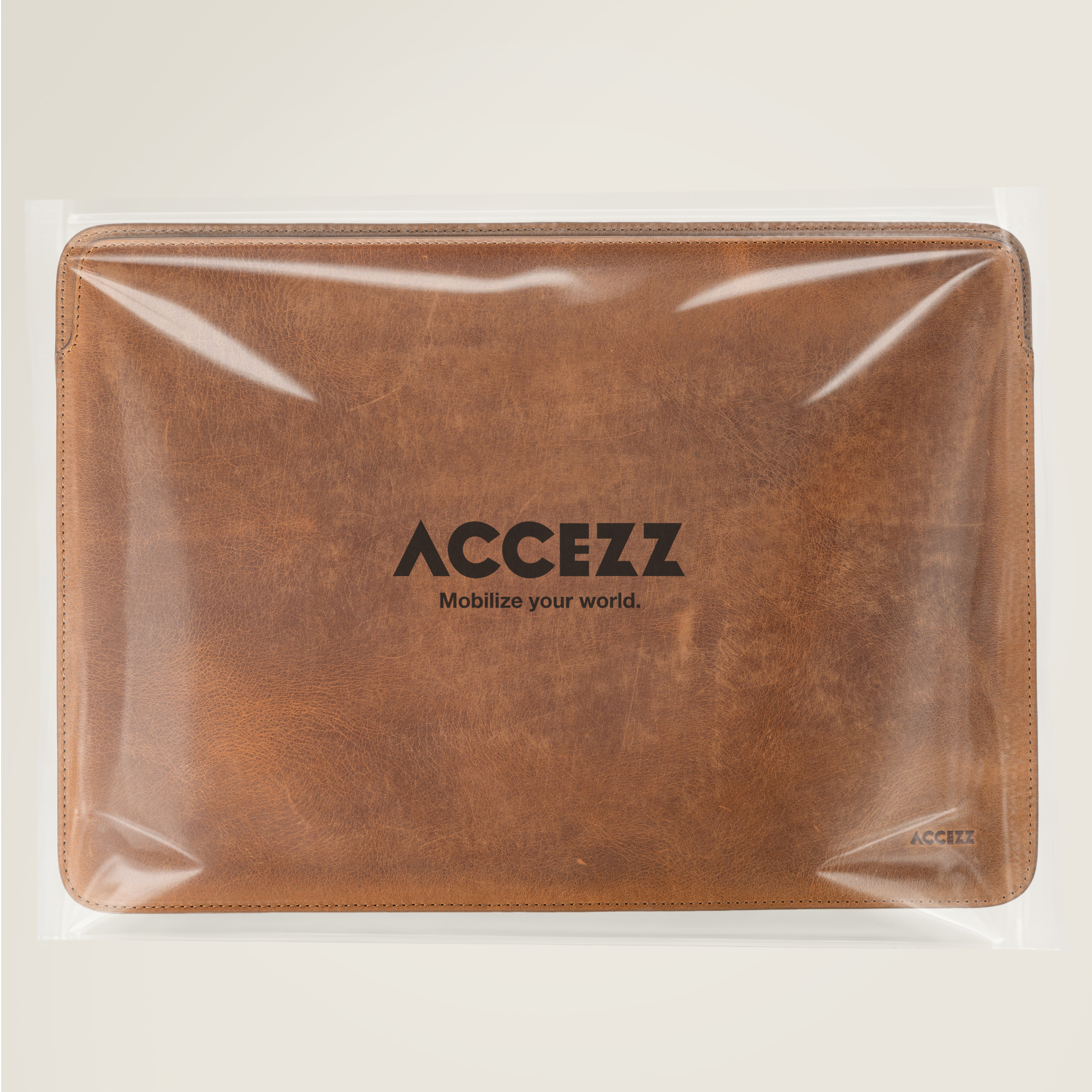 Brown leather laptop sleeve with ACCEZZ logo and slogan, in plastic packaging.