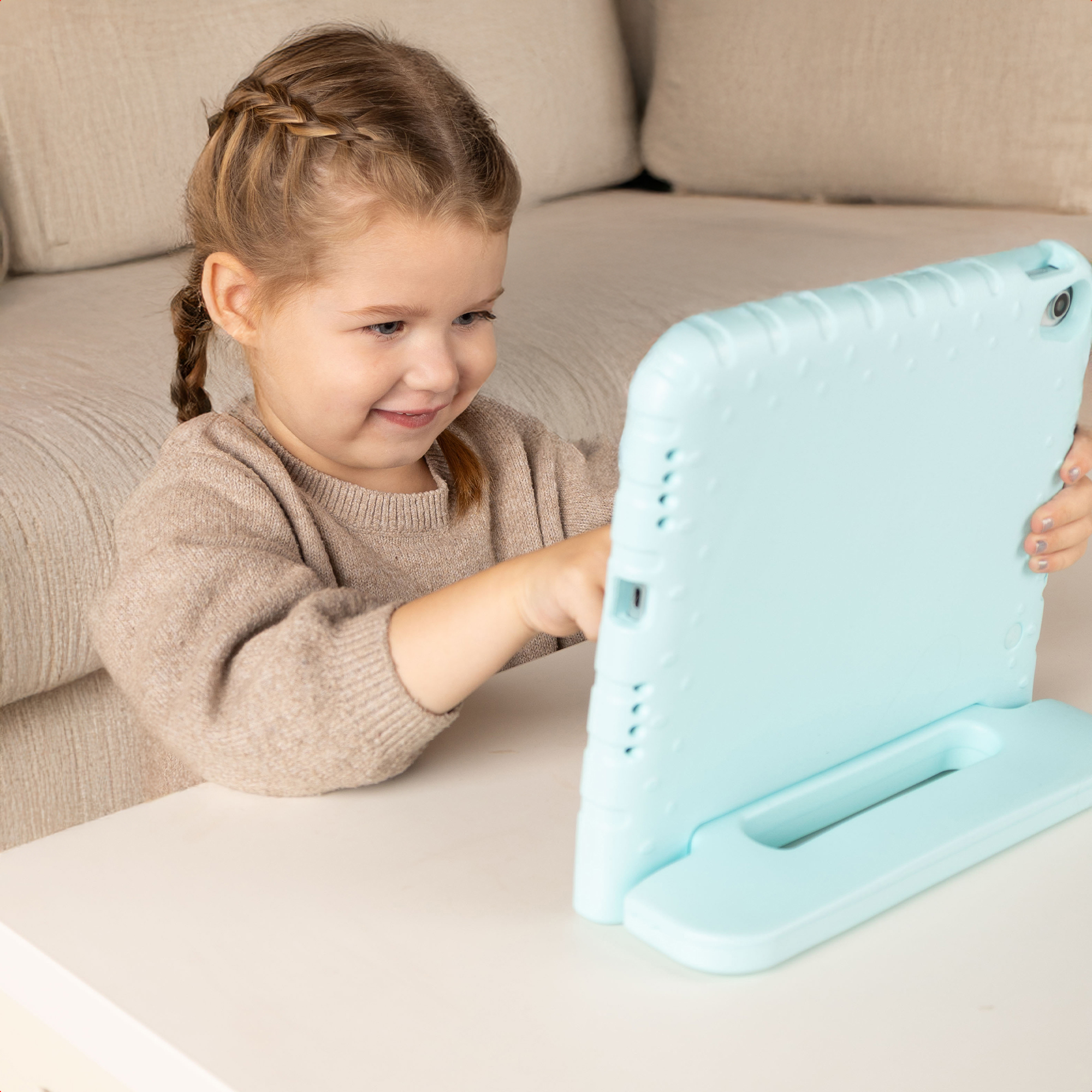 Une jeune fille aux cheveux tressés regarde une tablette vert menthe.