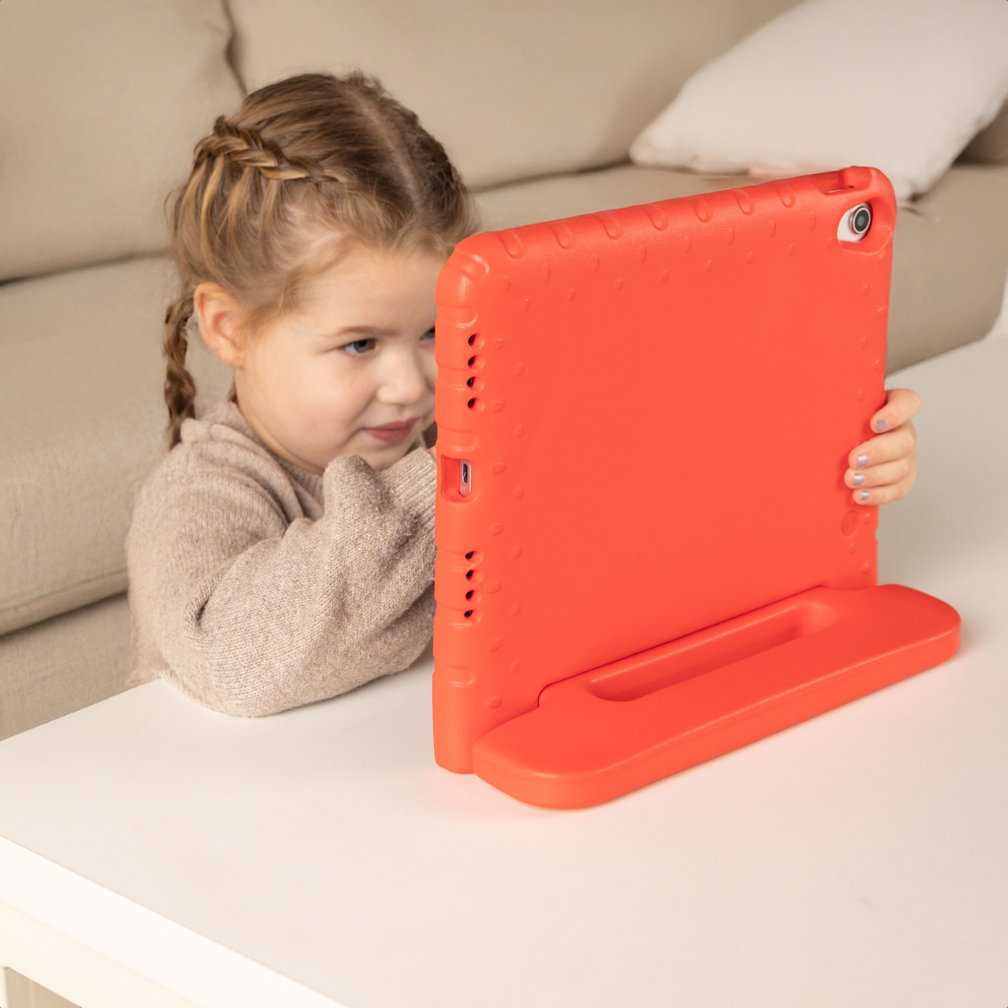 Une jeune fille aux cheveux tressés joue avec une tablette orange sur une table.