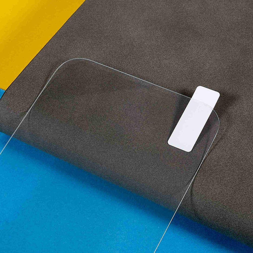 Ein transparenter Displayschutz mit weißem Klebestreifen liegt auf grauem und blauem Untergrund.