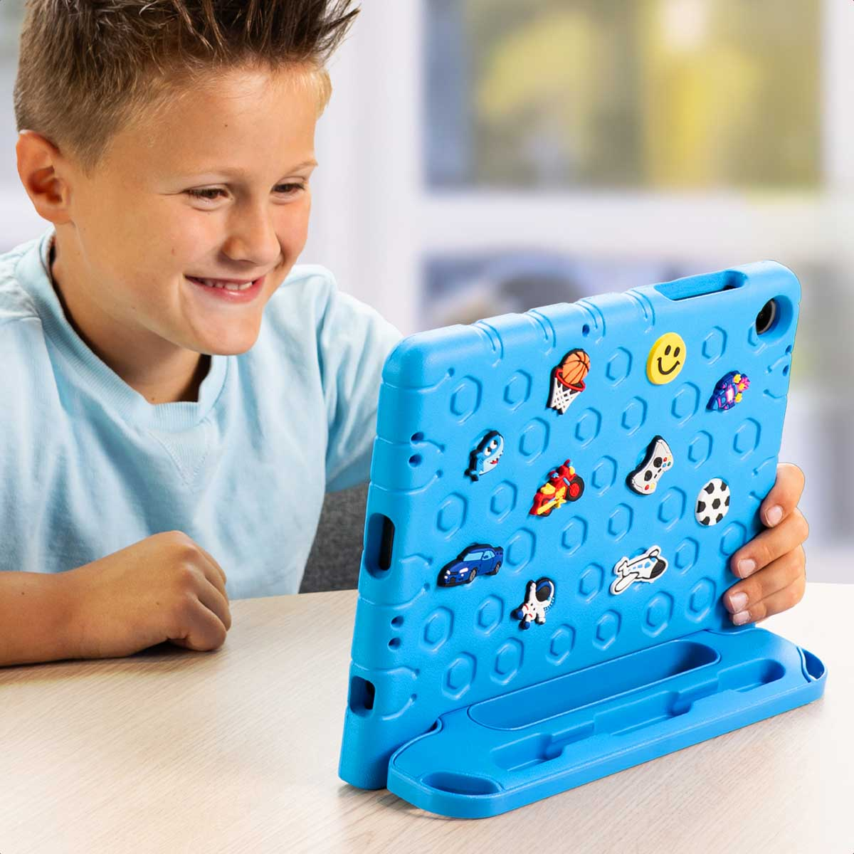 Un garçon sourit en tenant une tablette bleue avec des autocollants colorés.