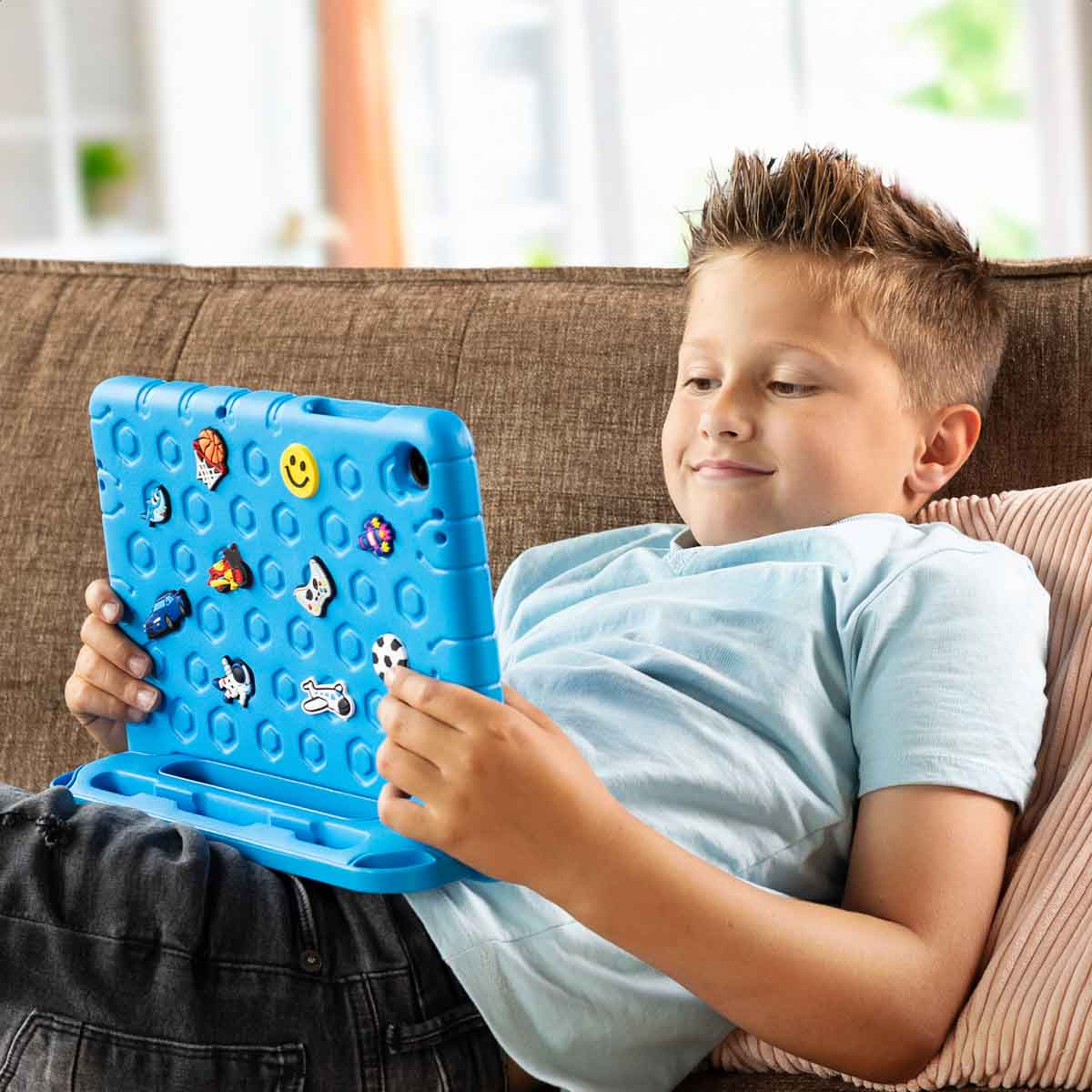 Un garçon est assis sur un canapé jouant avec une tablette jouet bleue ornée d'icônes.