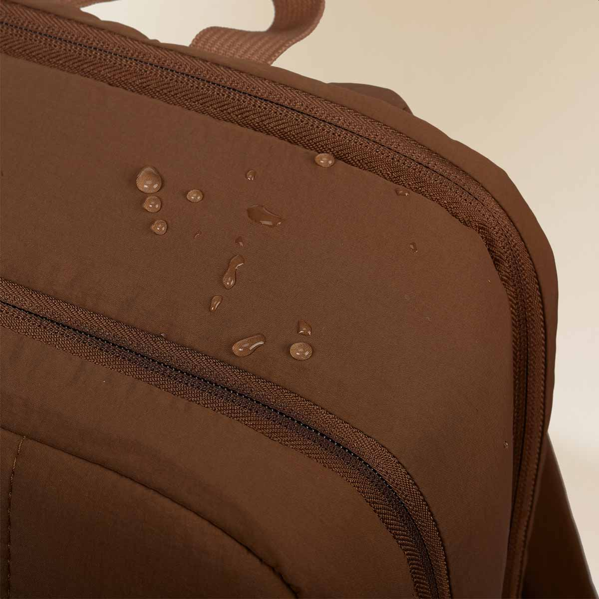 Brown fabric surface with zippers and water droplets.