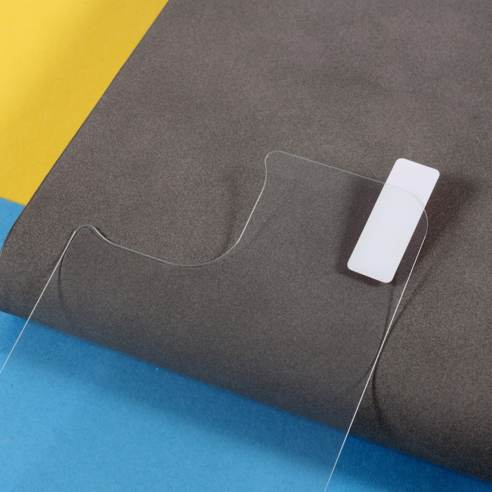 Un protecteur d'écran transparent avec un autocollant blanc repose sur un matériau gris, jaune et bleu.