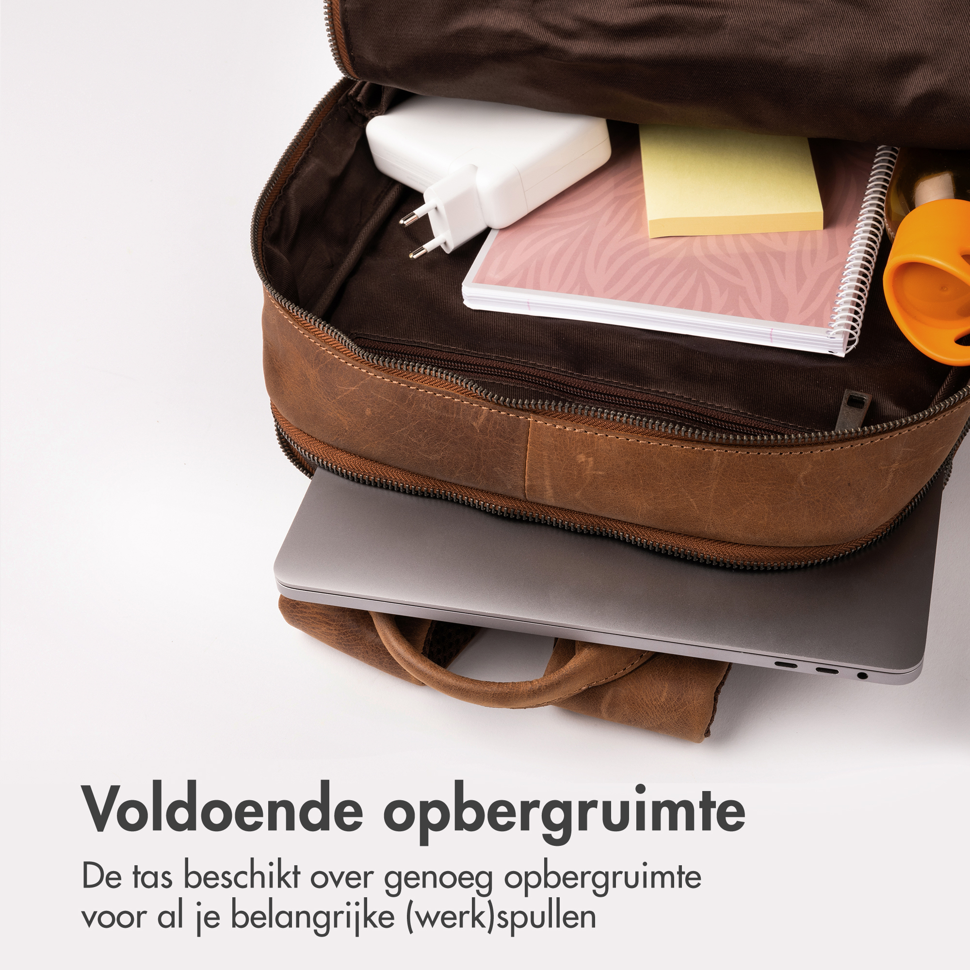 Bruine leren tas met laptop, oplader, notitieboek en mok.