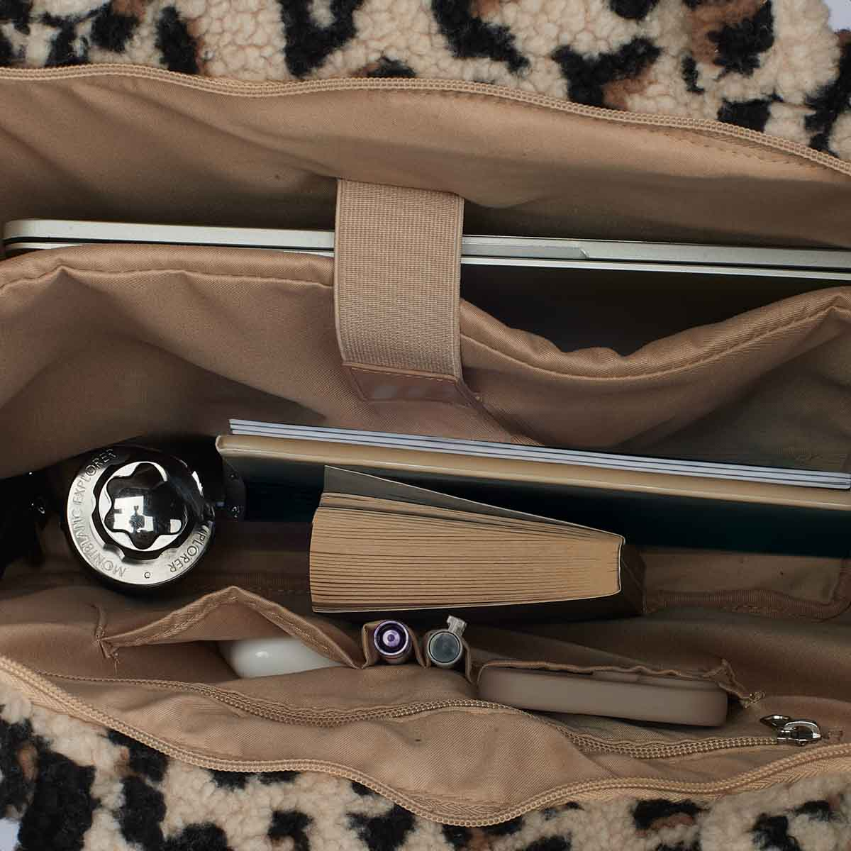 A leopard-print bag's interior holds a laptop, book, pens, and earbuds. Beige lining.