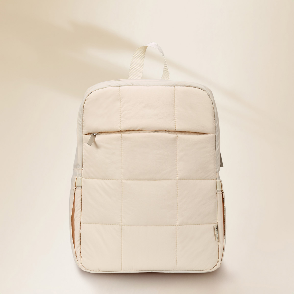A quilted, cream-colored backpack with zippers and a handle.