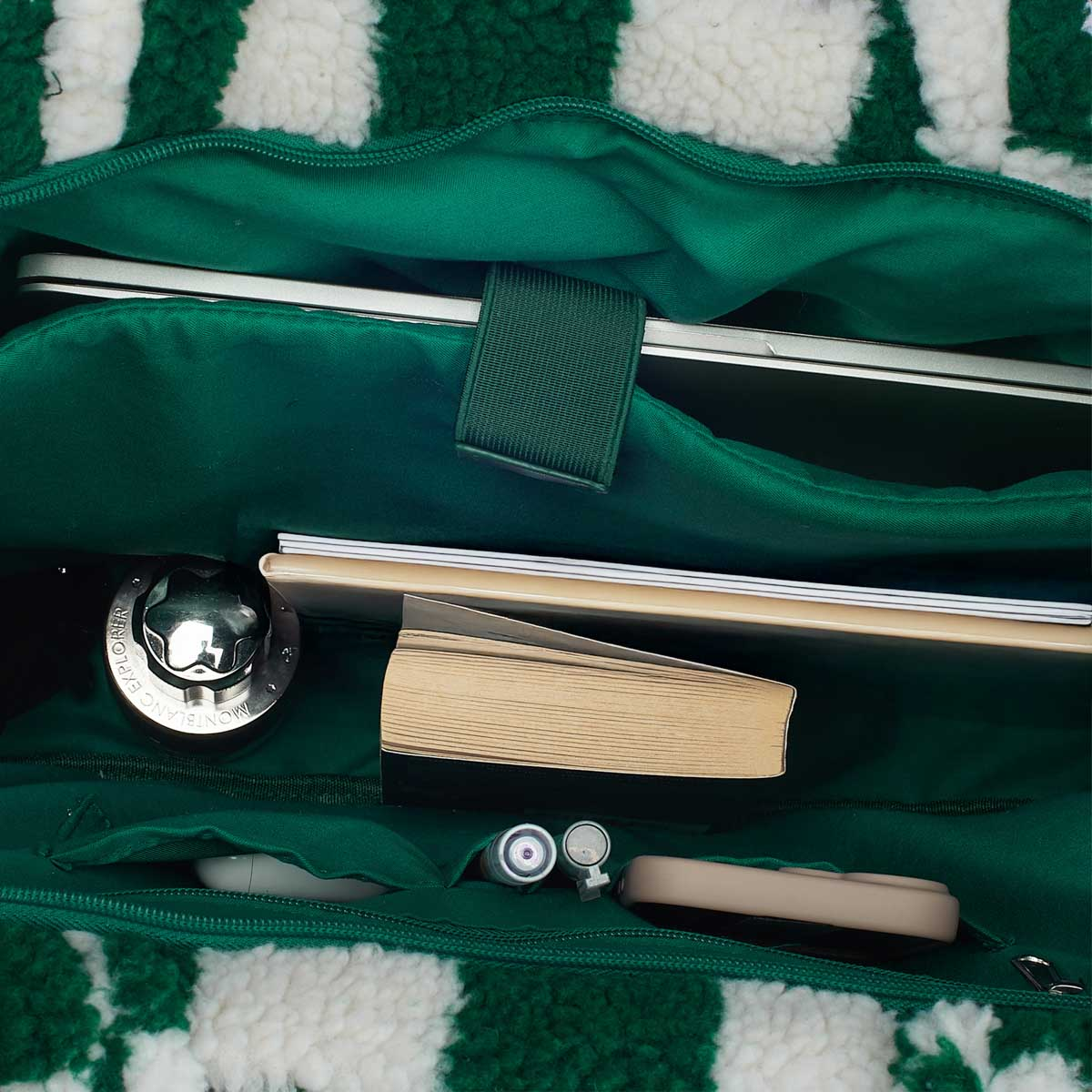 Green bag with white stripes, filled with a laptop, book, and cosmetics.
