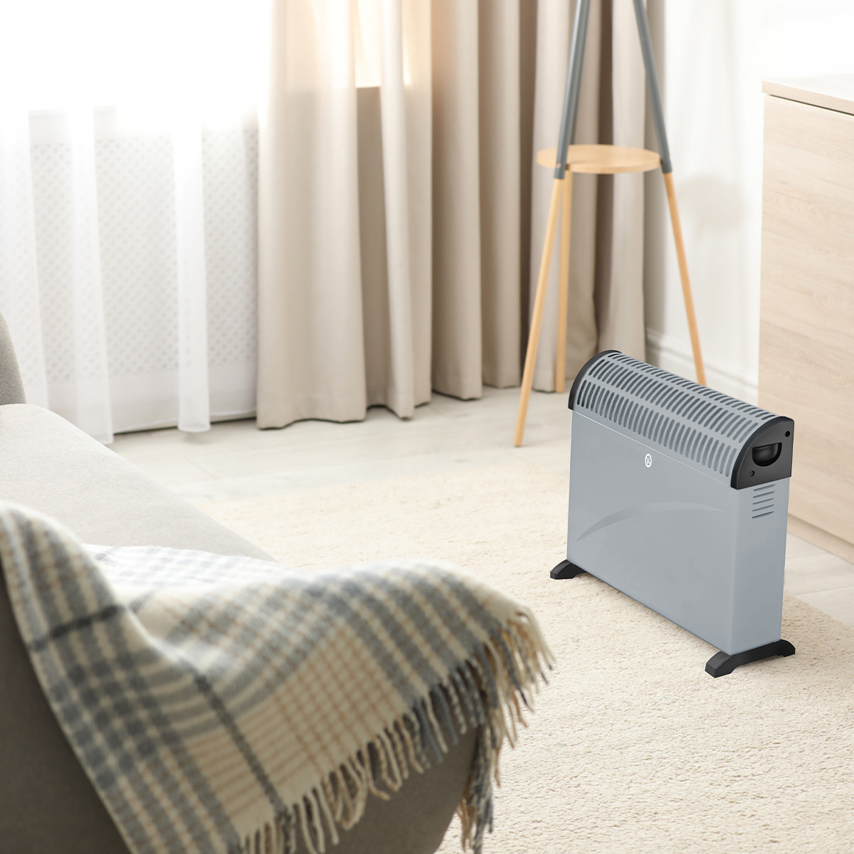 A grey heater sits on a rug in front of a window with curtains.