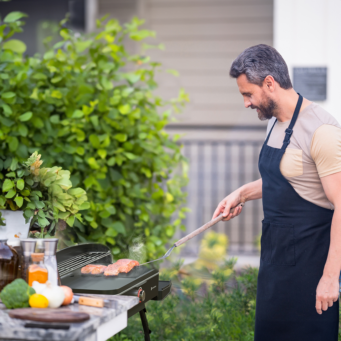 Man in black apron grilling salmon on an outdoor barbecue.