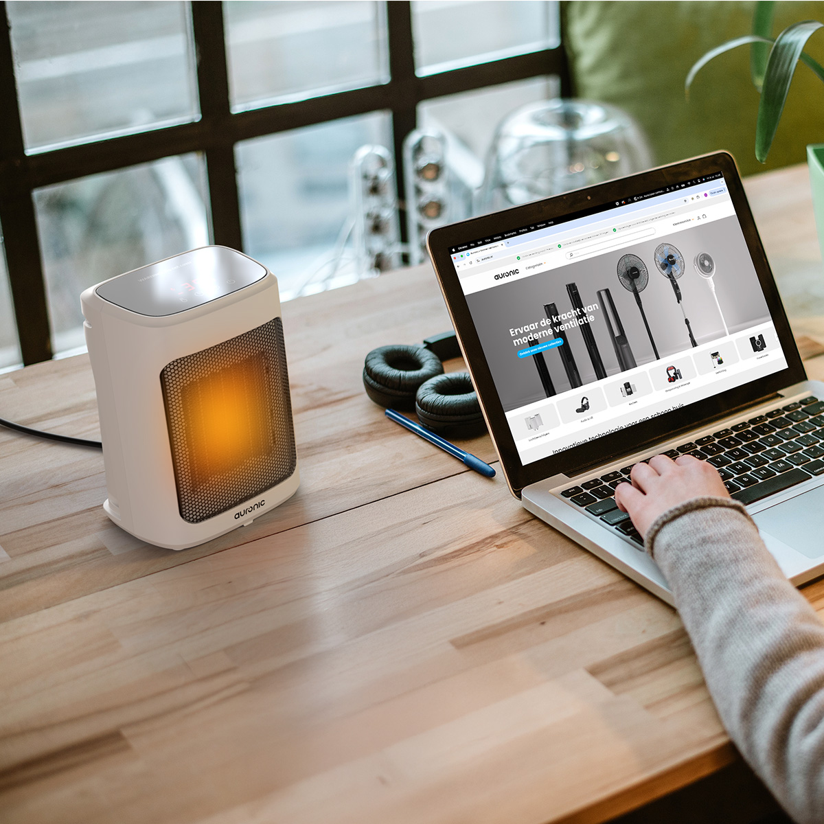 Un radiateur portable blanc brille chaudement à côté d'un ordinateur portable affichant des ventilateurs sur un bureau en bois.