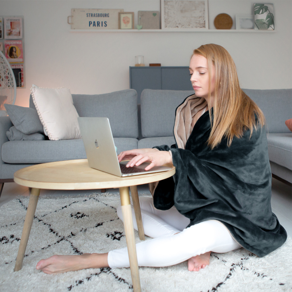A woman sits on the floor using a laptop, wrapped in a blanket.
