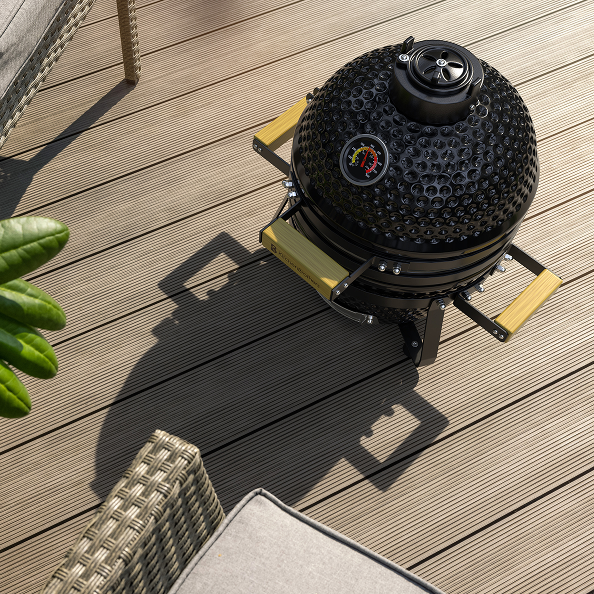 Zwarte keramische grill met houten handvatten op houten vlonder, naast fauteuil.