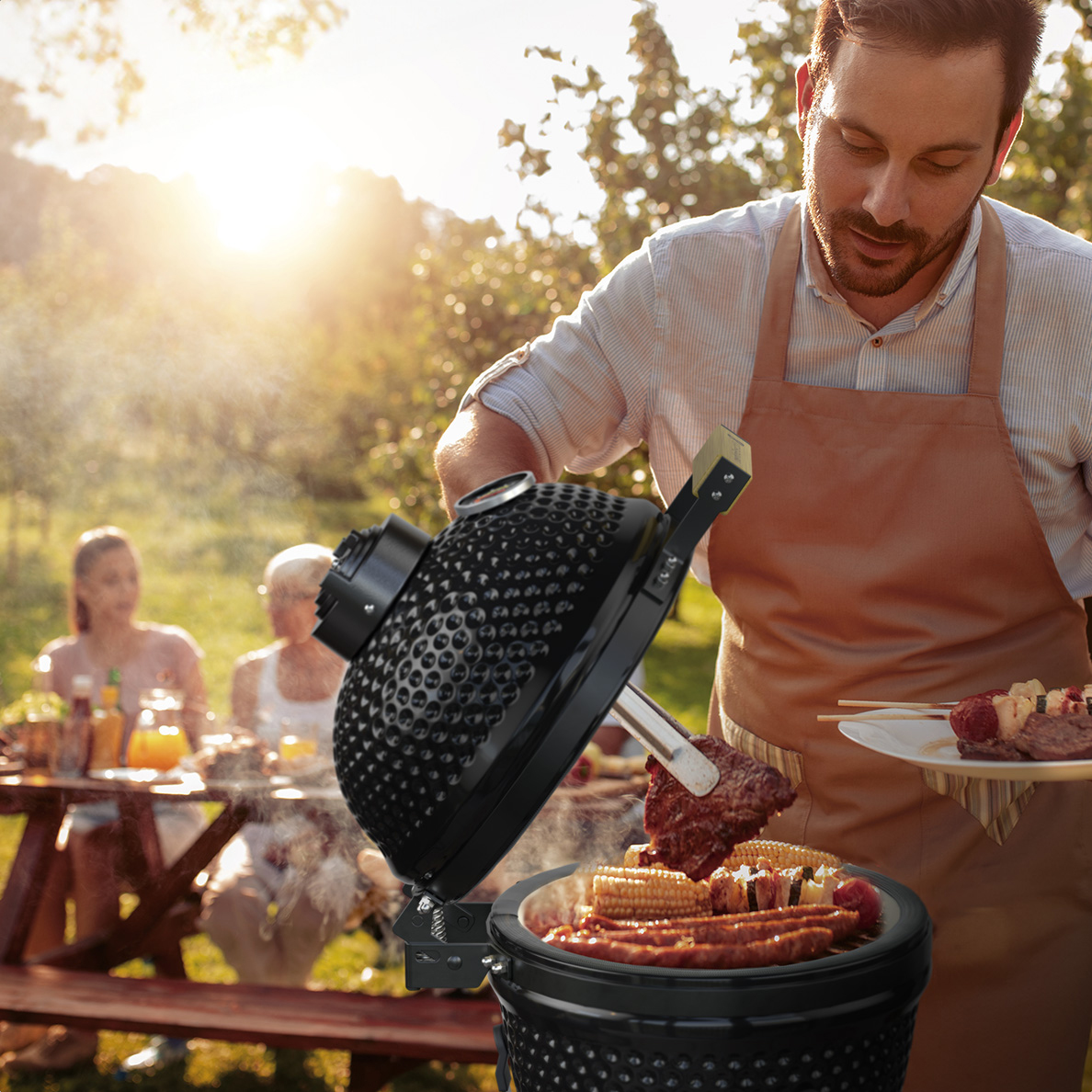 Un homme grille de la viande et des épis de maïs à l'extérieur, famille au fond.