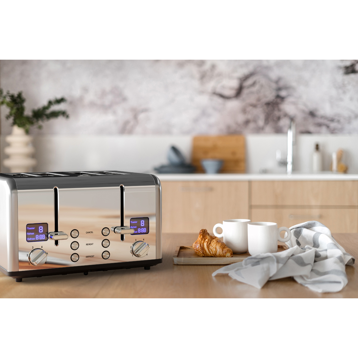 A shiny toaster with digital displays sits on a wooden table with two cups and a croissant.