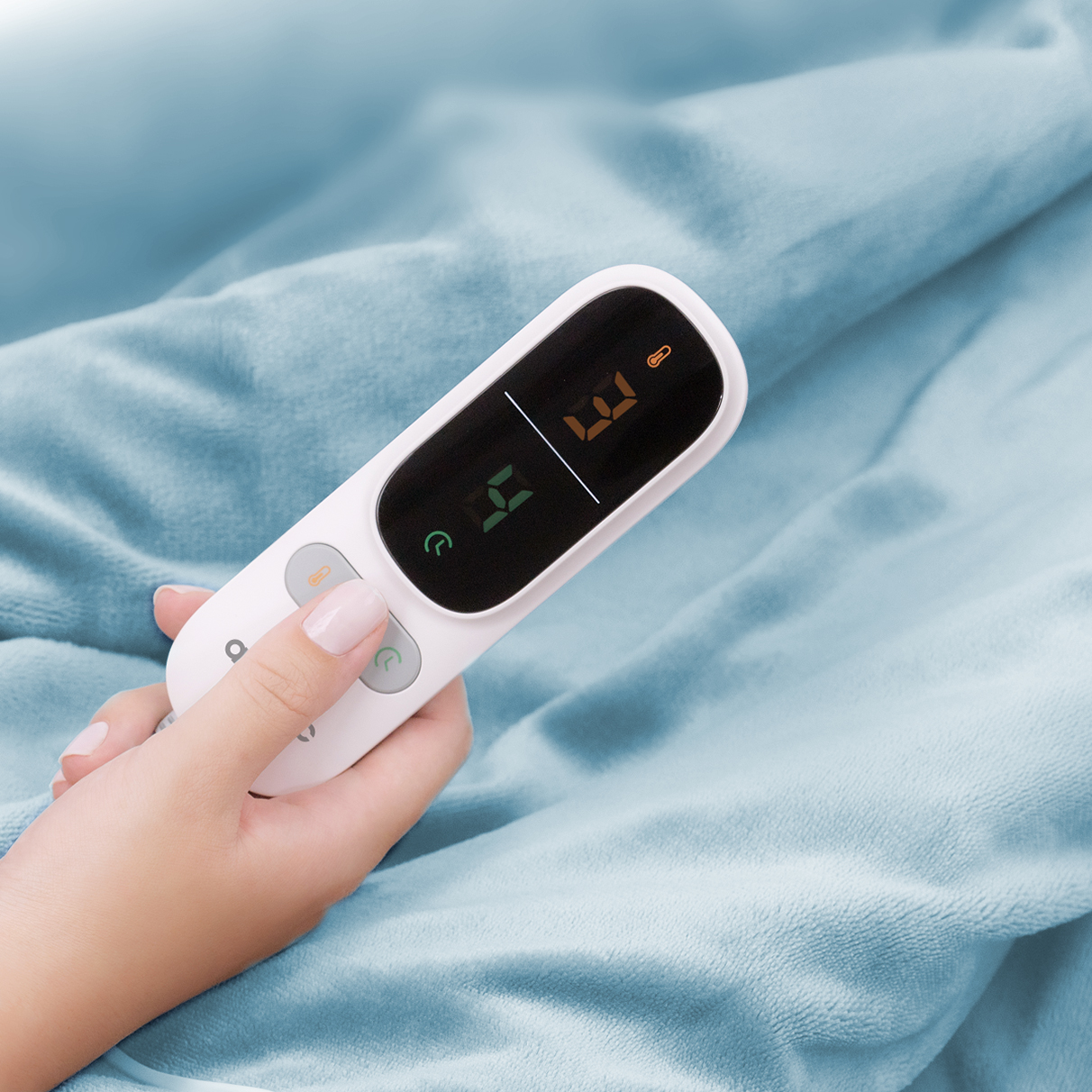 A hand holds a white thermometer with a digital display on blue fabric.