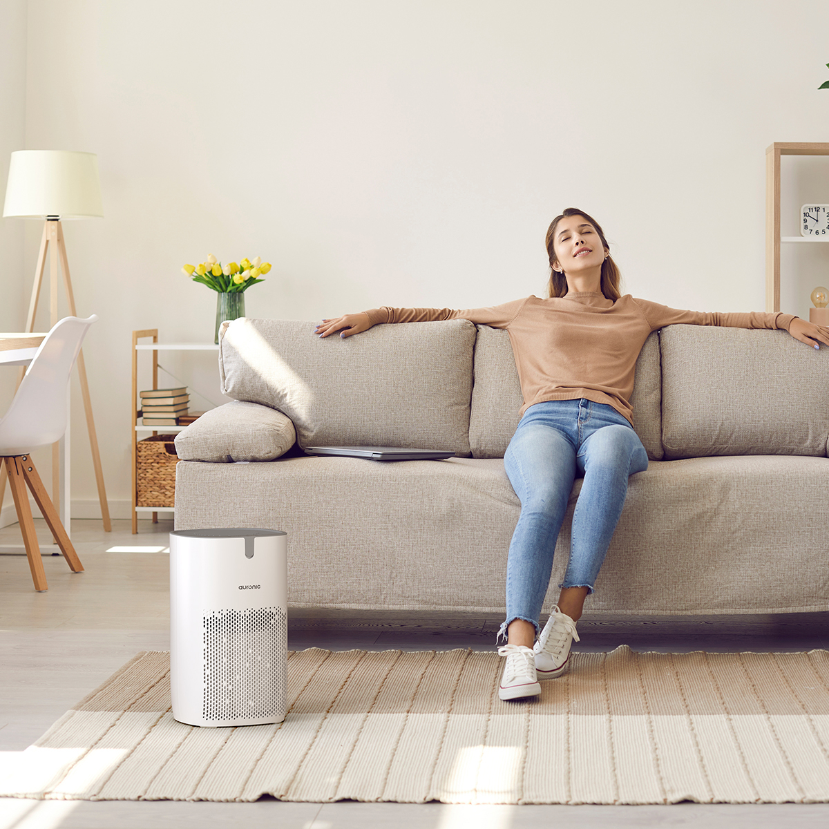 Woman relaxing on sofa, air purifier nearby. Bright room with desk.