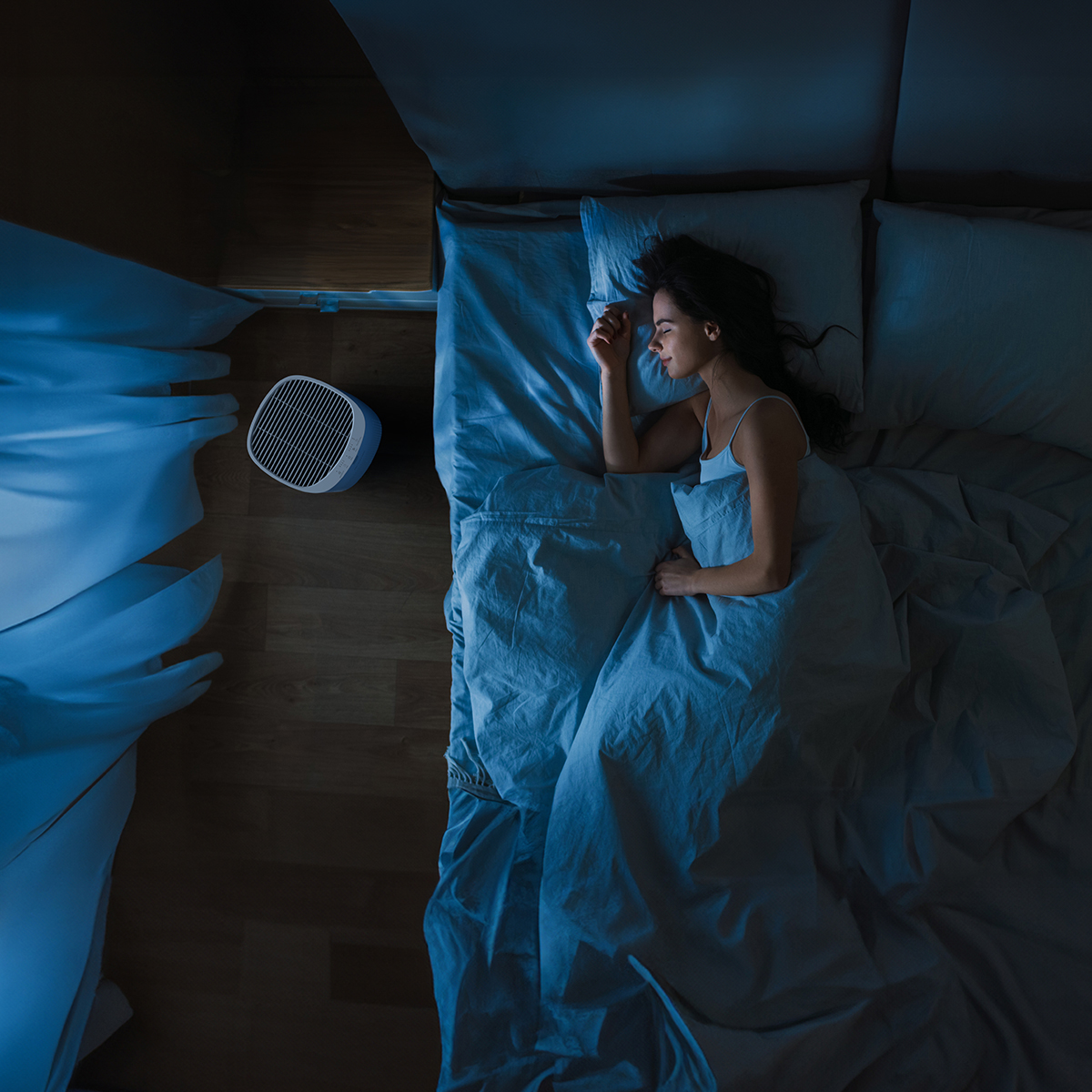 A woman sleeps in bed with an air purifier nearby.