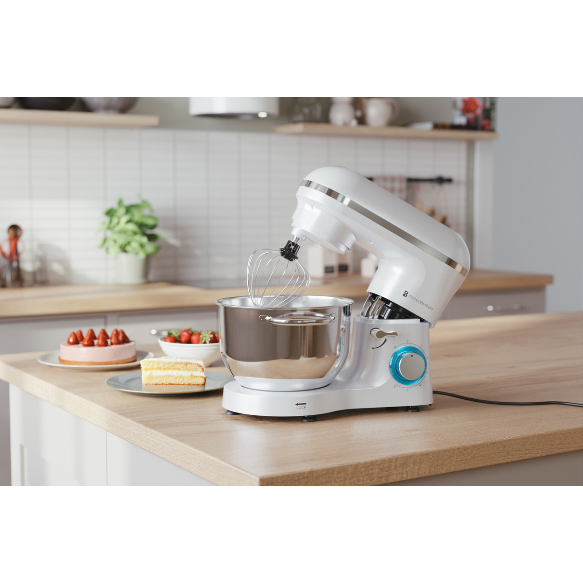 Un robot pâtissier blanc avec fouet est sur un comptoir en bois à côté de gâteaux et de fraises.