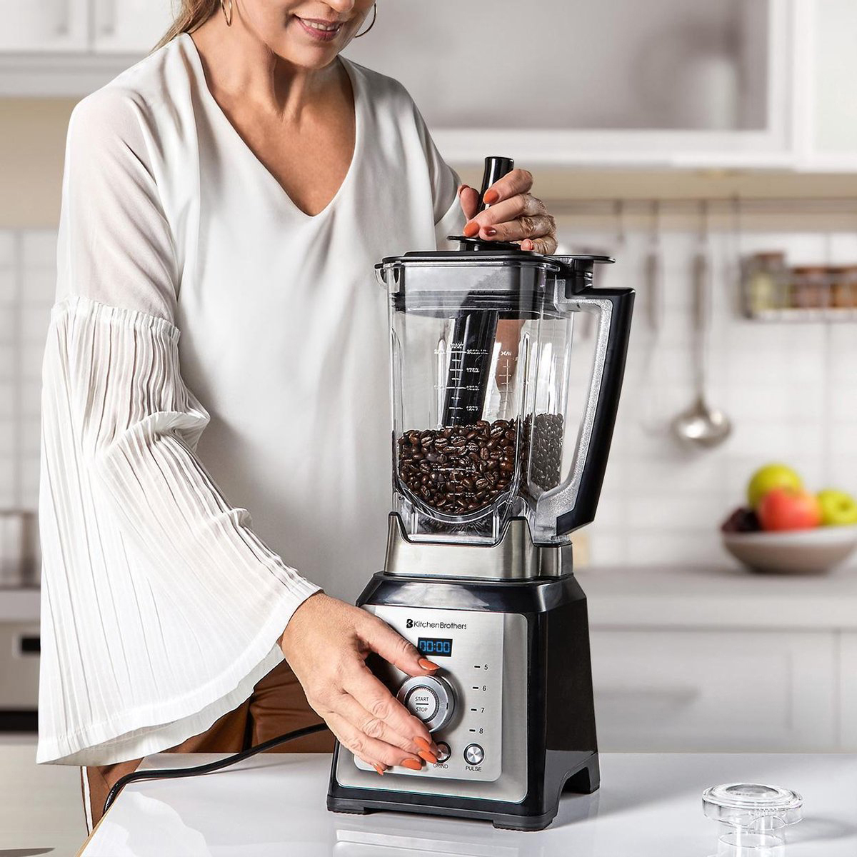A woman in a white blouse uses a blender filled with coffee beans.