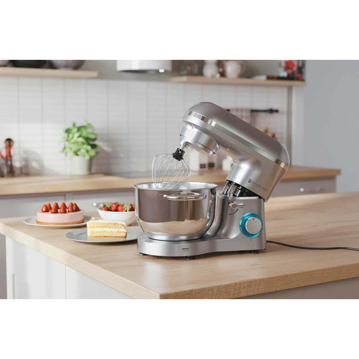 Een zilveren standmixer met mengkom en garde staat op een houten aanrecht.