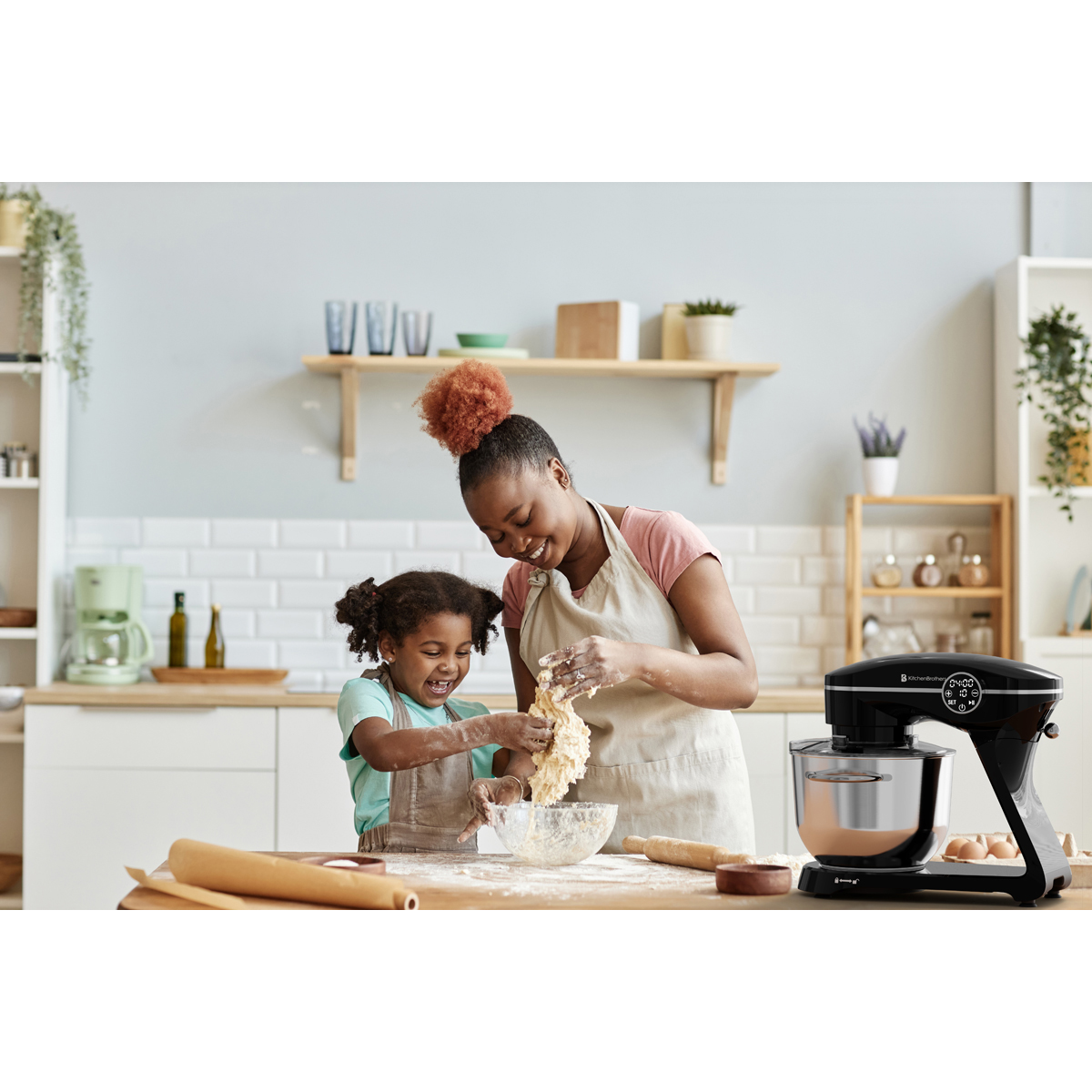 Mère et fille pétrissent de la pâte dans une cuisine près d'un robot pâtissier.