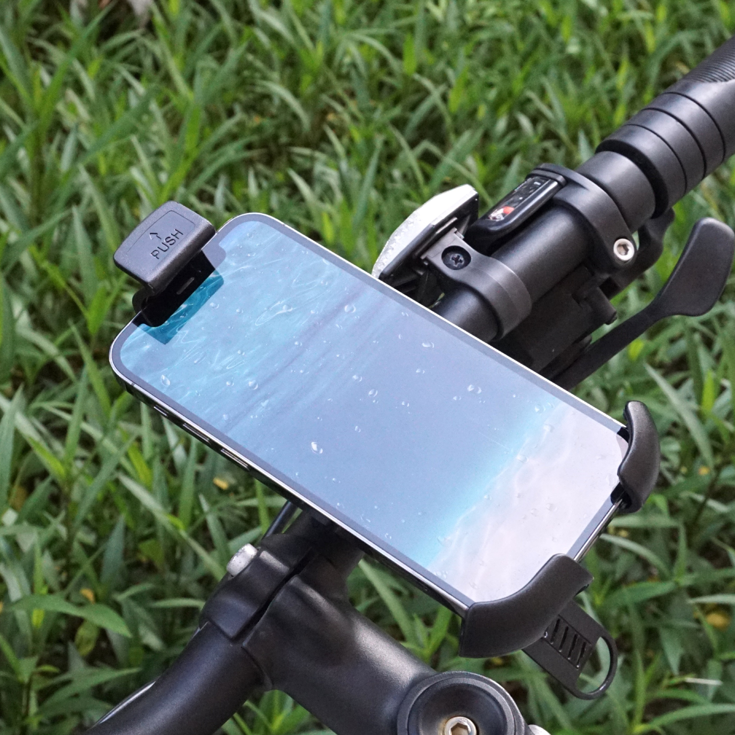 Smartfon w uchwycie na kierownicy roweru, z zieloną trawą w tle.