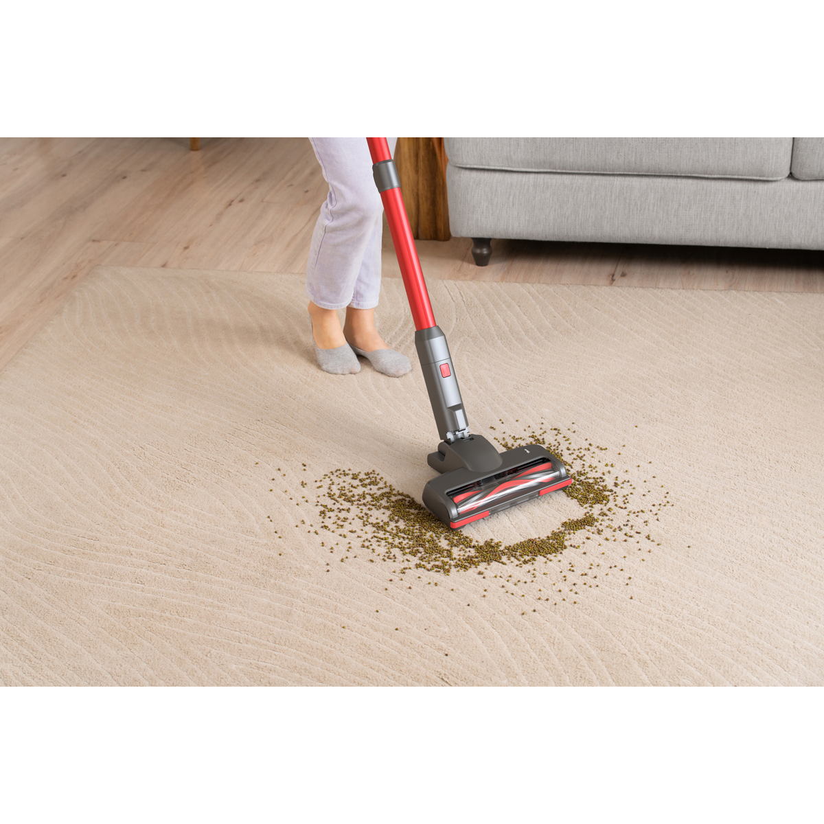 Une personne passe l'aspirateur sur des haricots verts dispersés sur un tapis beige avec un aspirateur rouge et gris.