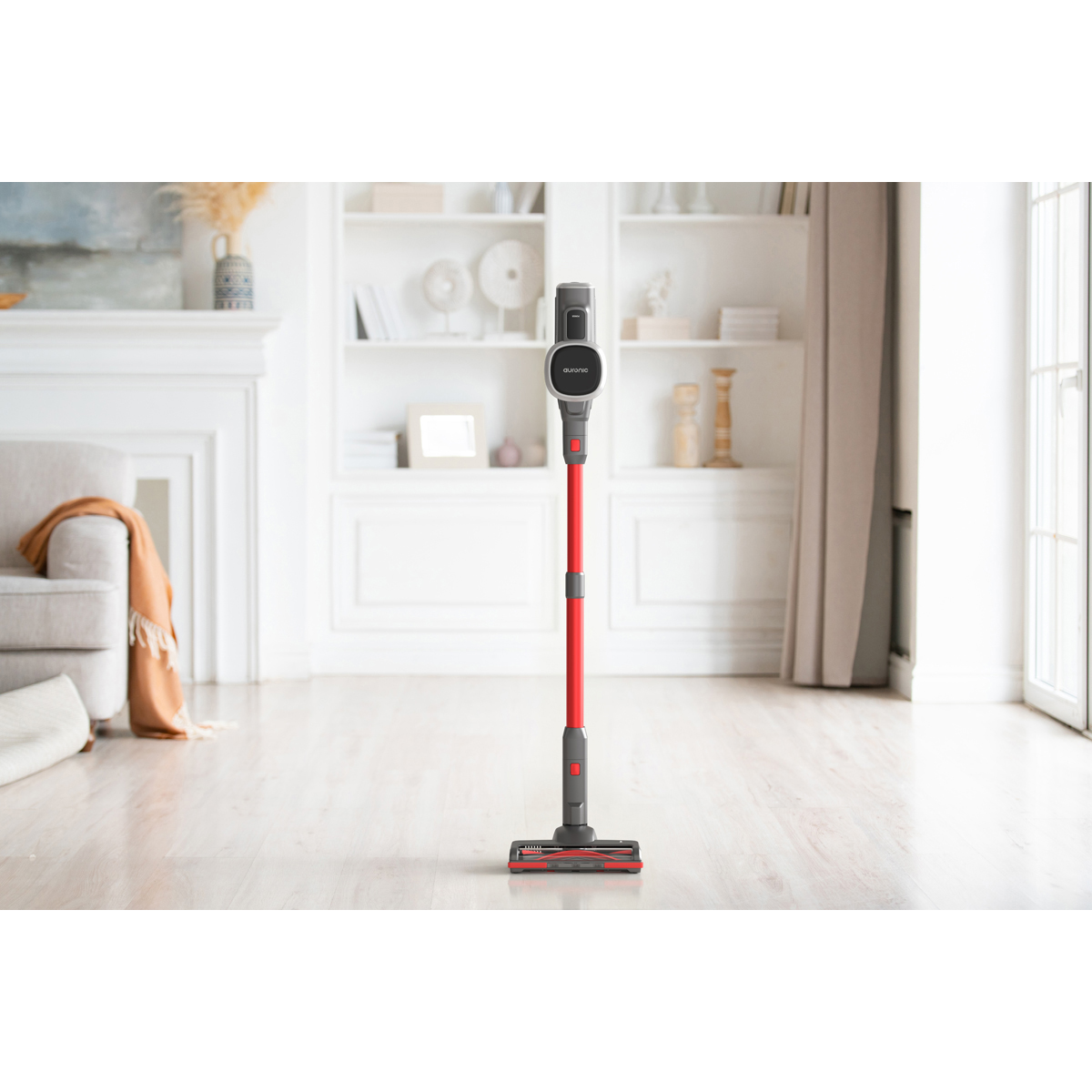 Un aspirateur sans fil rouge et gris sur un plancher en bois.