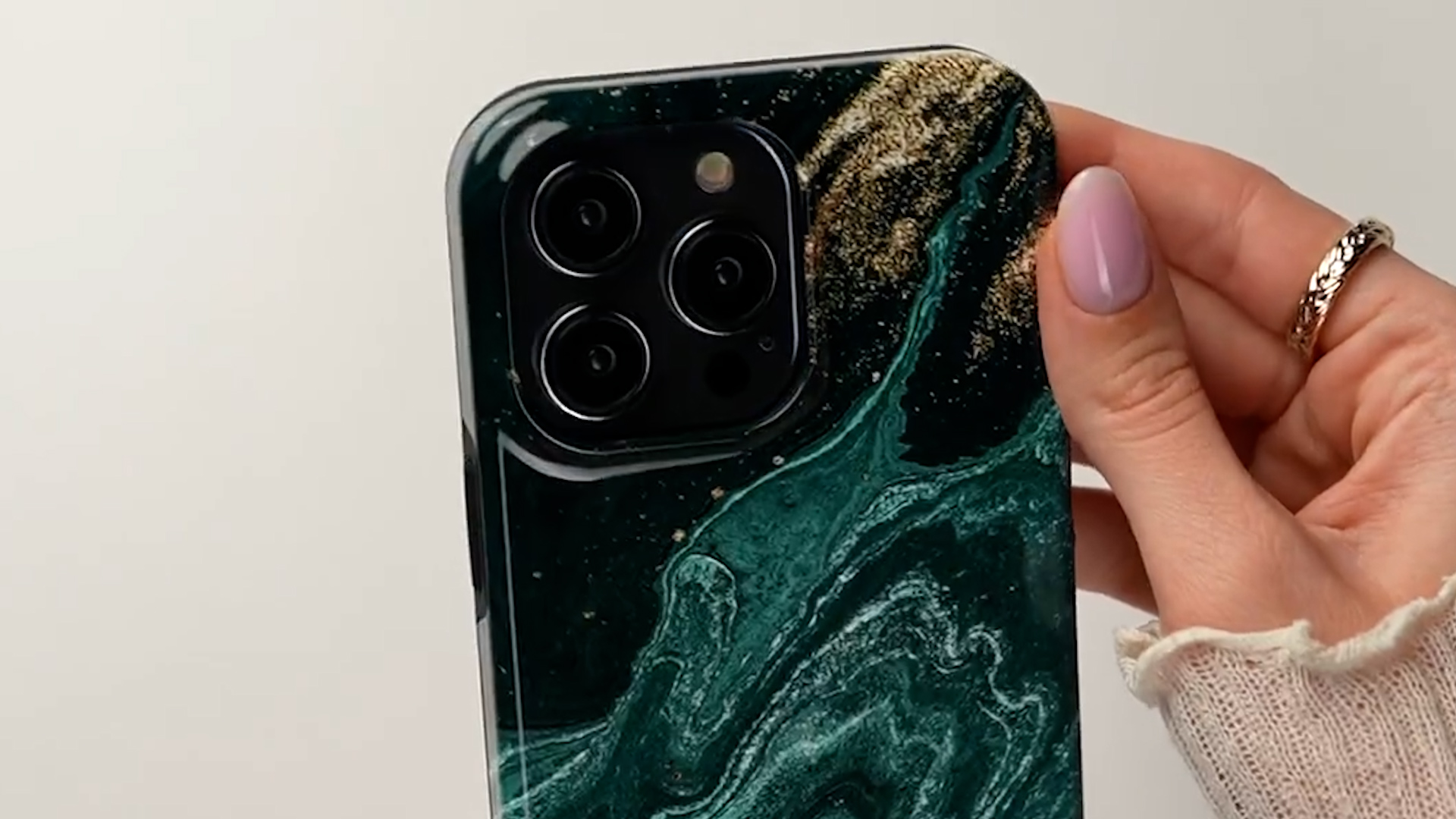 Een hand houdt een telefoon vast met een donker marmerpatroon en gouden spikkels.