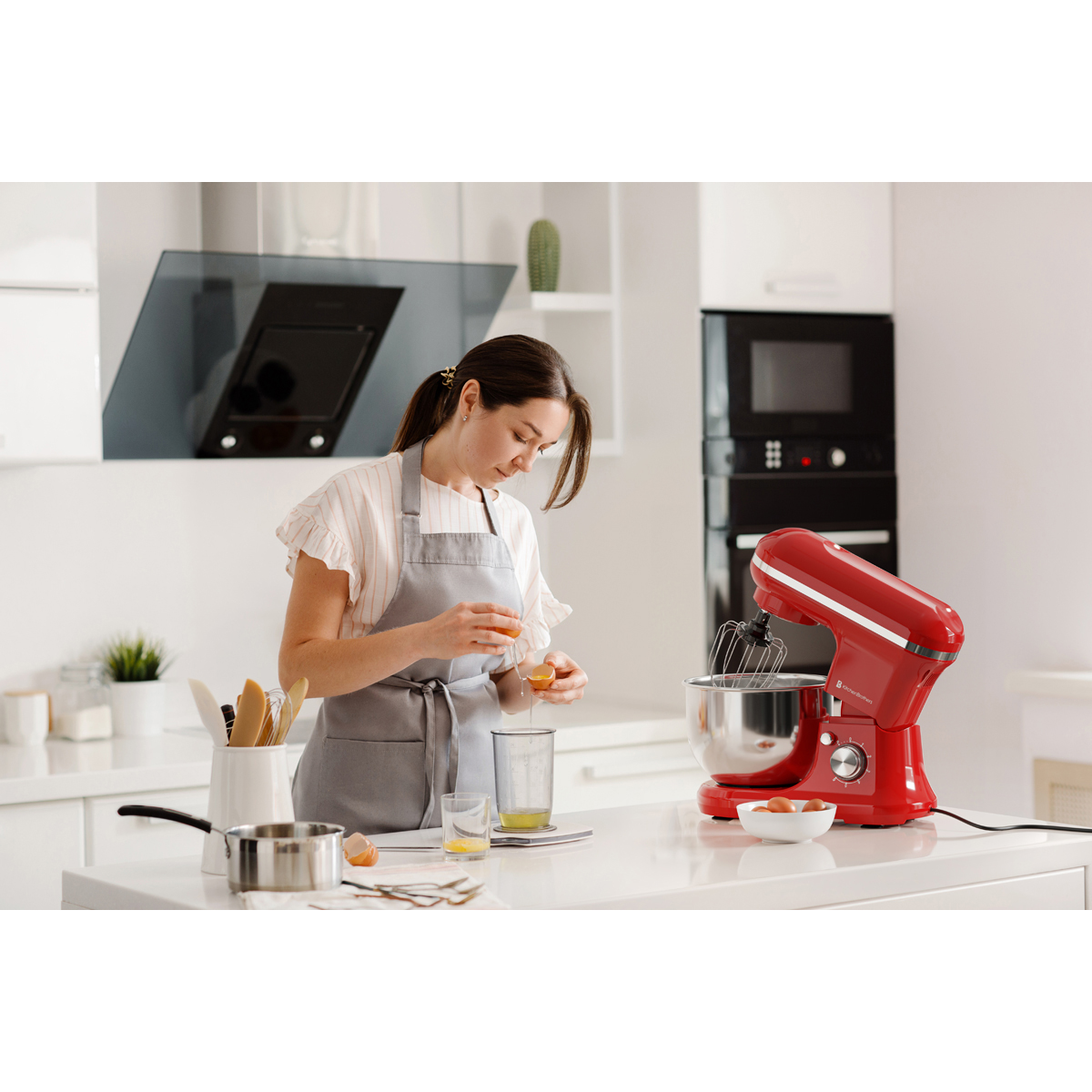 Een vrouw met schort scheidt eieren in een moderne keuken naast een rode standmixer.