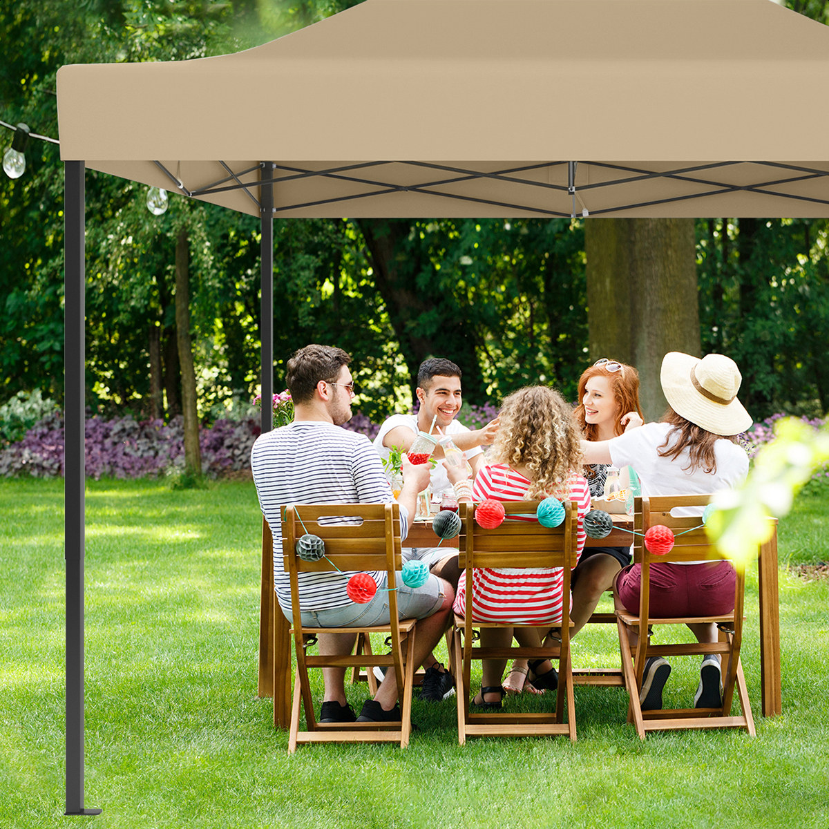 Five people sit at a wooden table outdoors under a tan canopy.