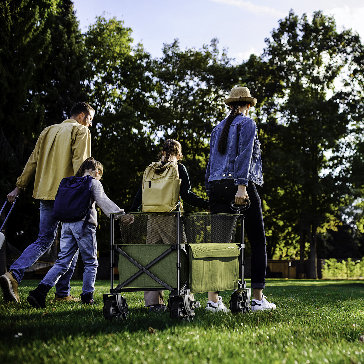 A family pulls a green wagon across a sunny, grassy field.