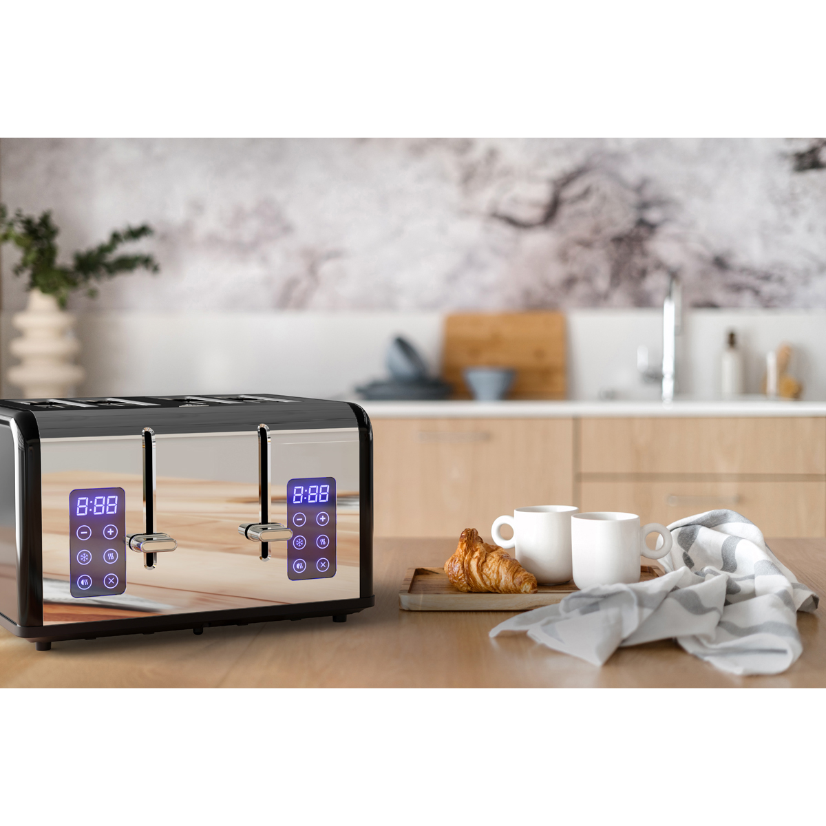 A shiny toaster with digital displays sits on a wooden table. Two cups and croissants are nearby.