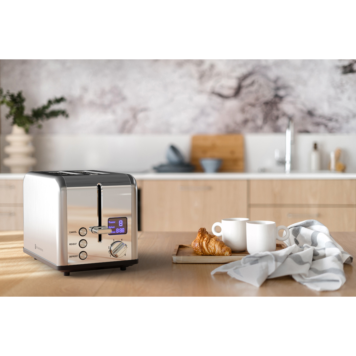 A modern chrome toaster sits on a wooden table with two croissants and cups.
