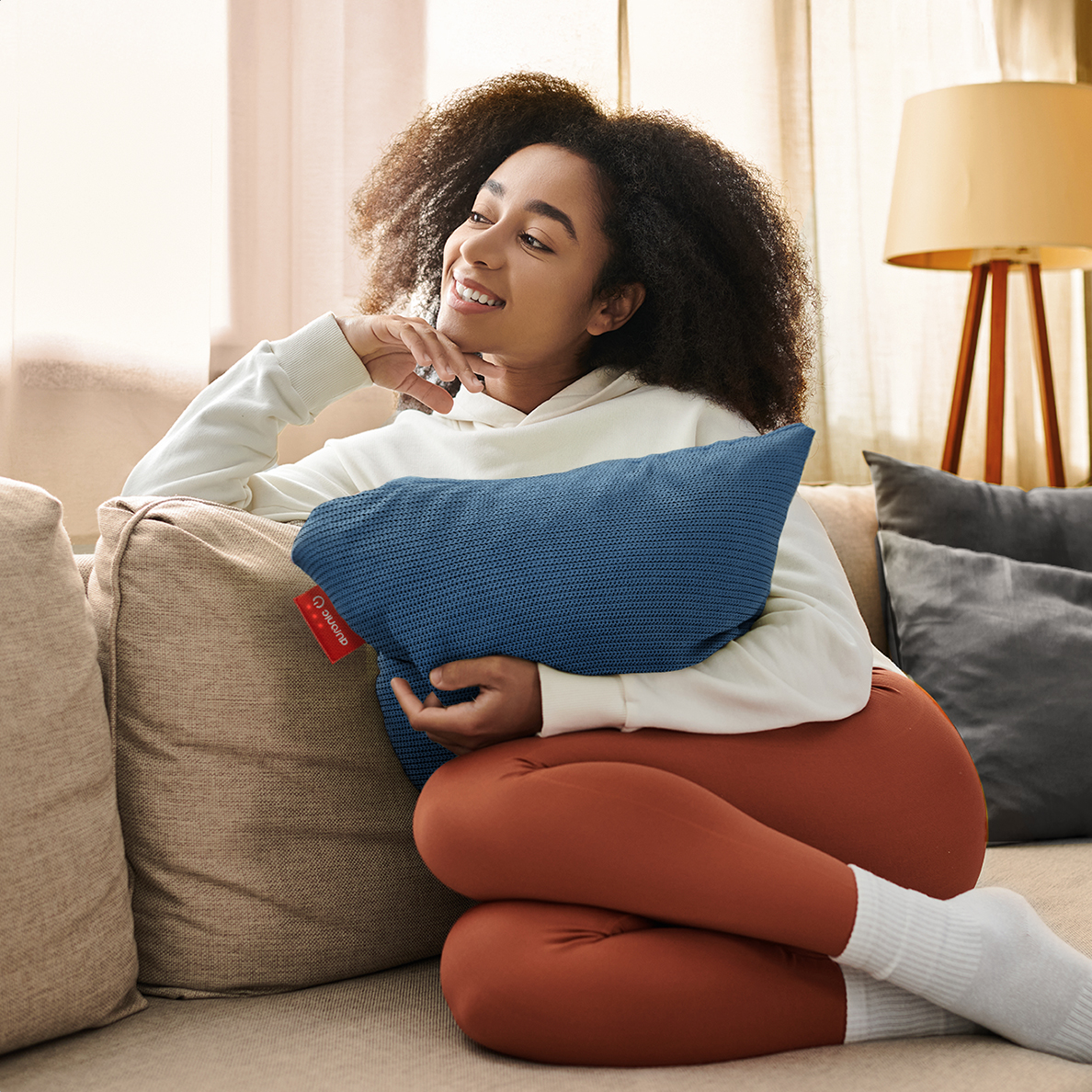 Une femme aux cheveux bouclés est assise sur un canapé, tenant un coussin bleu.