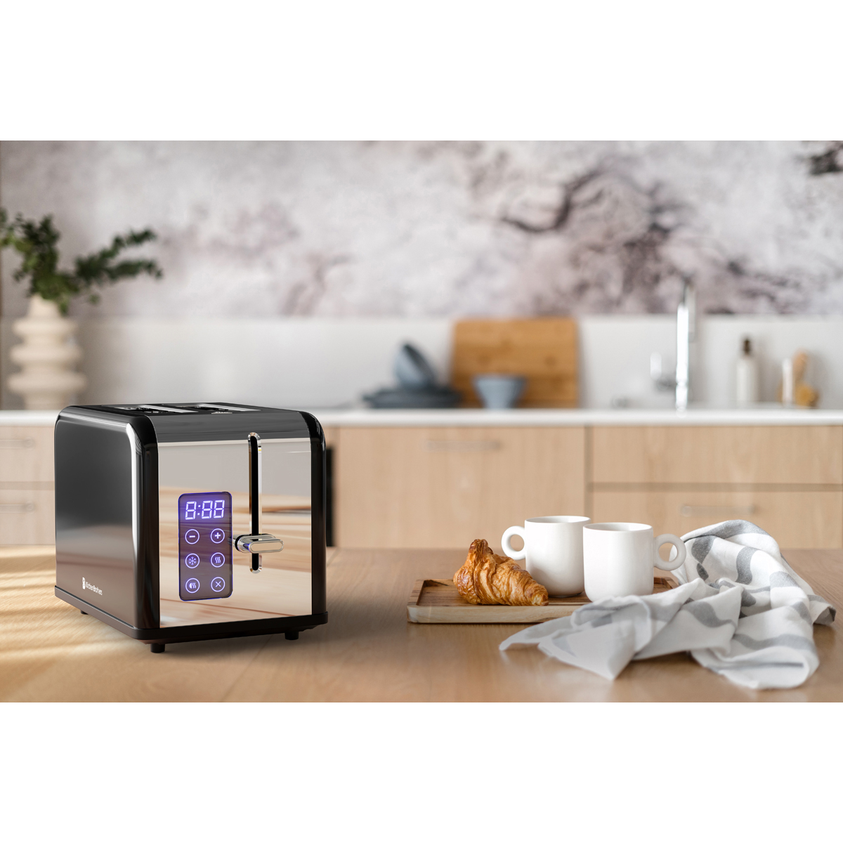 A black toaster with a digital display sits on a wooden table next to two cups and a croissant.