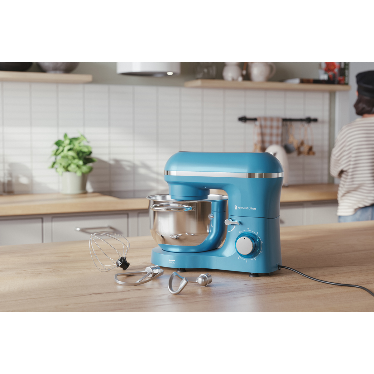Een blauwe keukenmixer met roestvrijstalen kom en accessoires op een houten aanrecht.