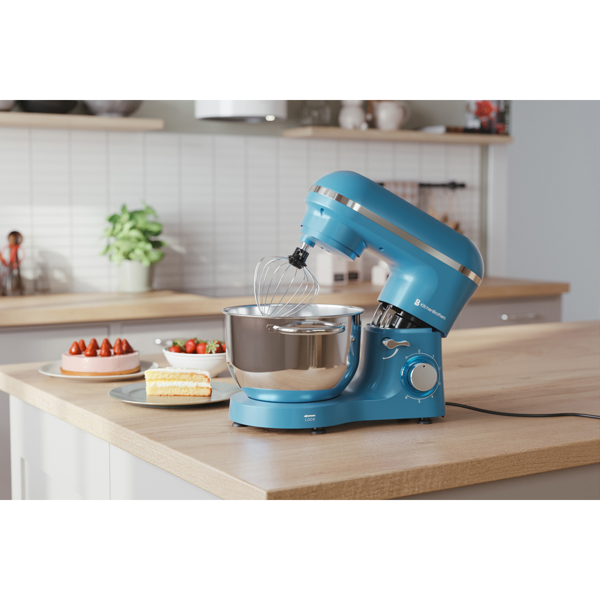 Een blauwe keukenmixer staat op een houten aanrecht naast cake en aardbeien.